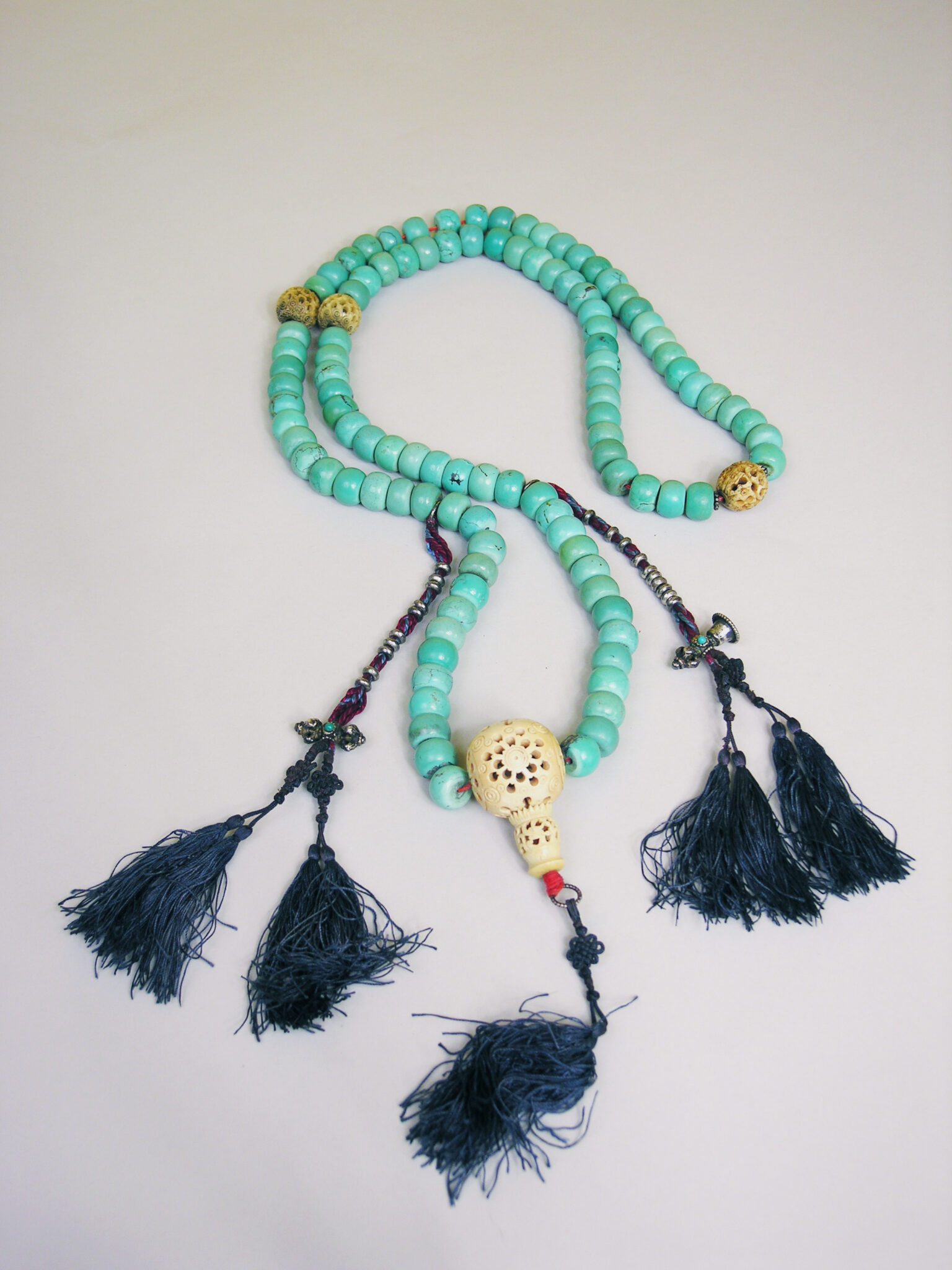 Loosely arranged string of turquoise beads with carved bone centerpiece and five dark-blue tassels