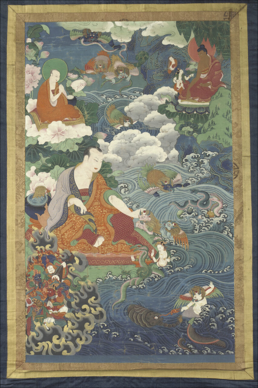 Monk seated at bank of rushing river extends right hand to serpent deities swimming in water