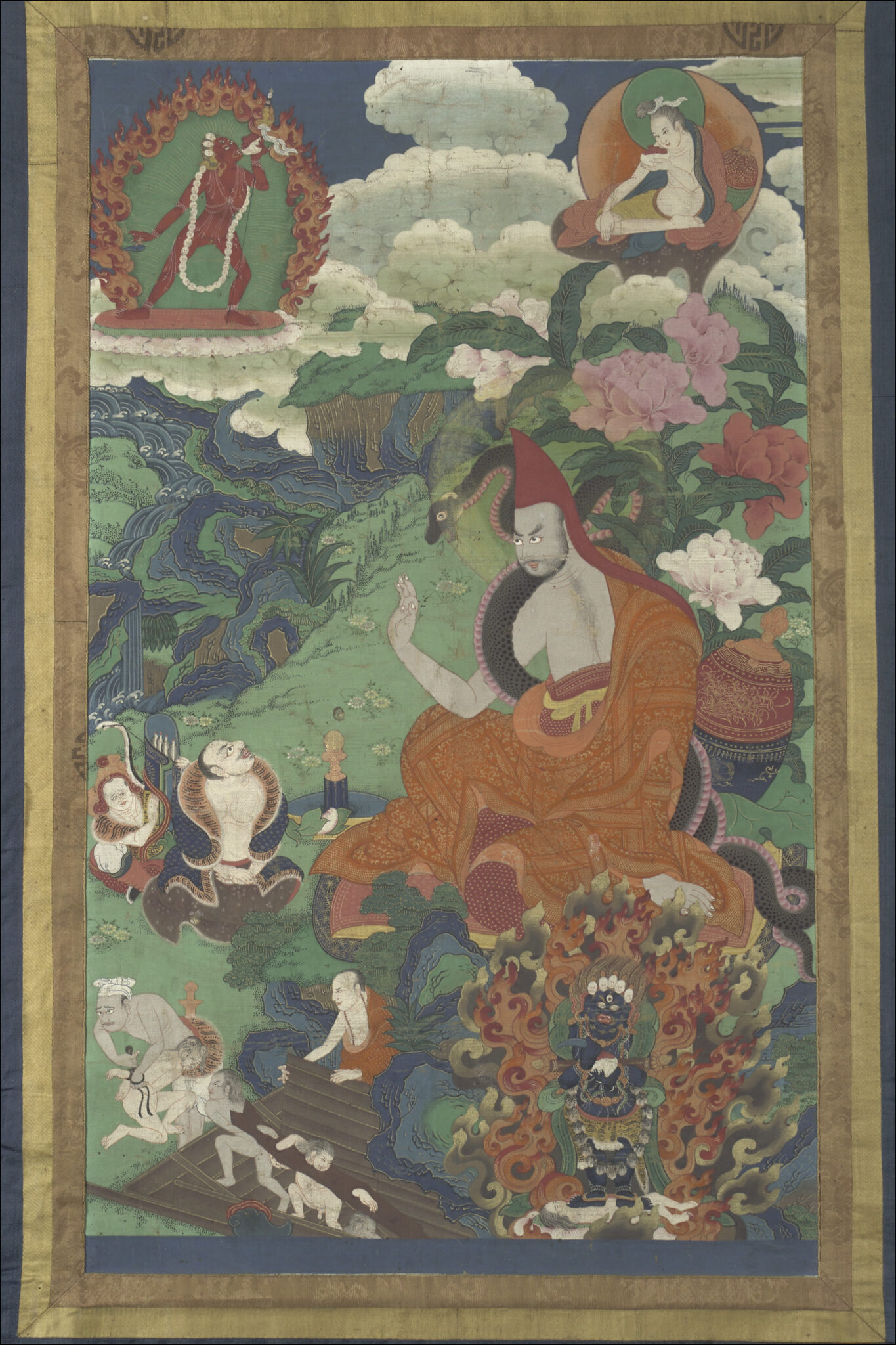 Monk in brilliant orange robe with serpent at left shoulder gestures with left hand against menacing figures at left