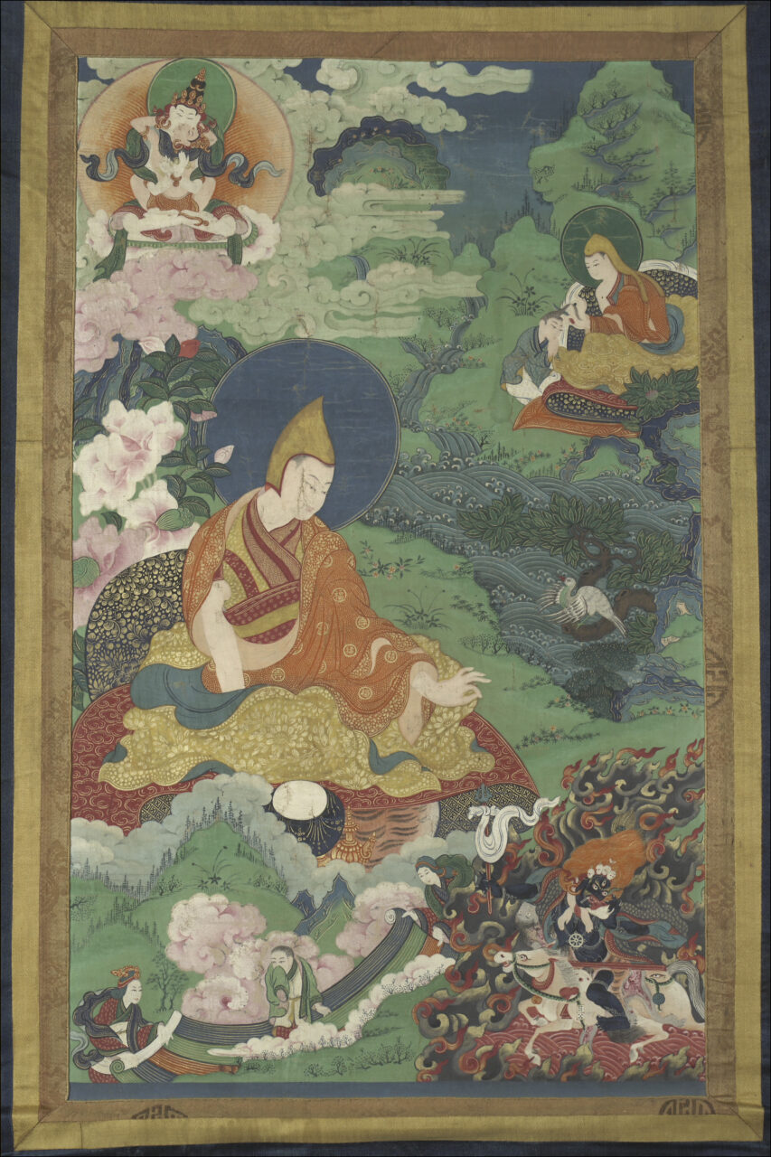 Lama wearing resplendent saffron robe extends right hand in mudra towards wrathful deity at bottom right