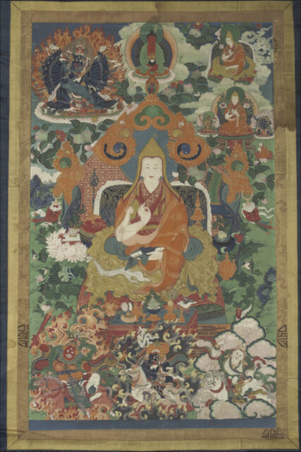 Lama seated on throne with orange cloud-motif backrest amidst portraits of Buddha, wrathful deities, and lamas