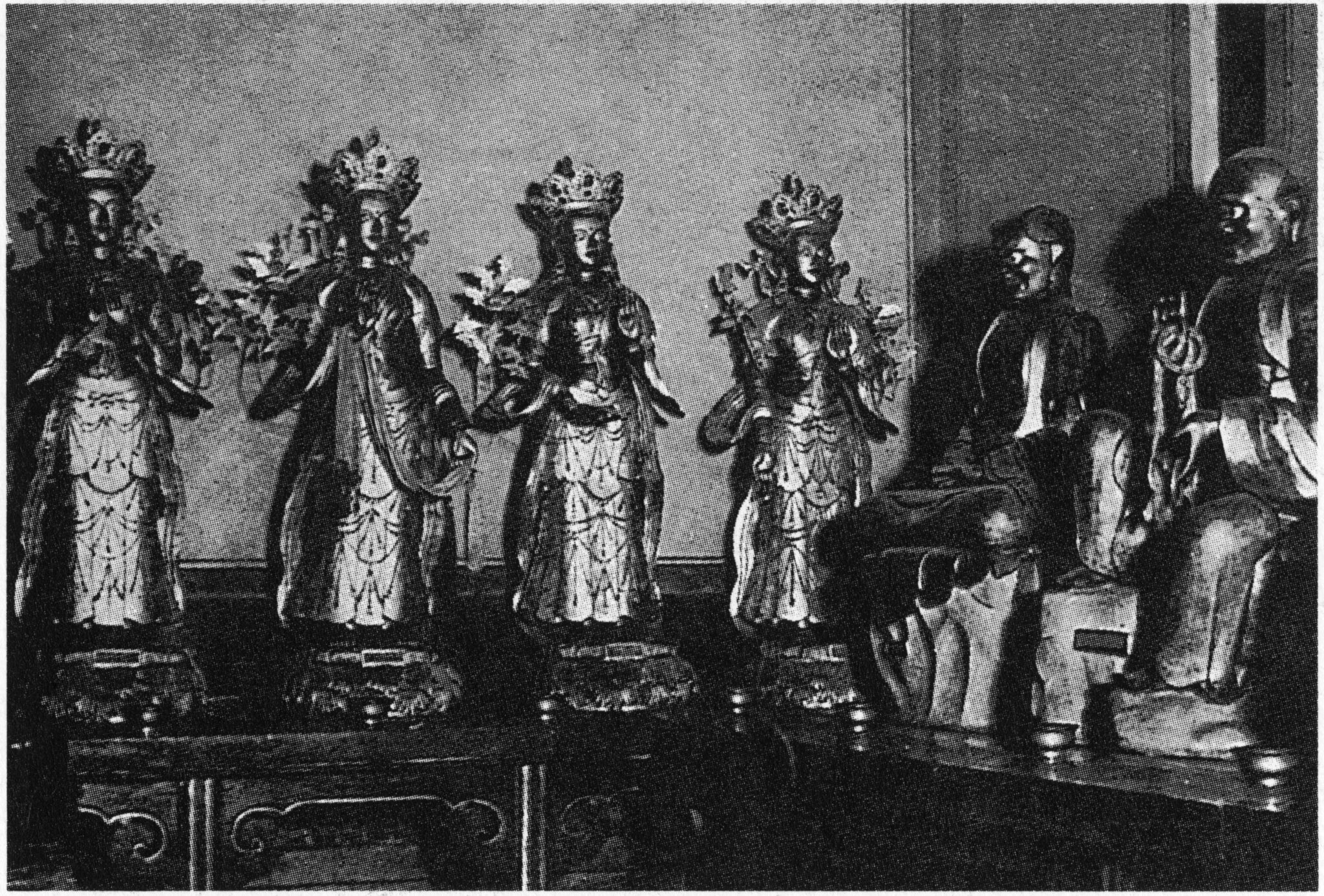 Black and white photograph of six statues, four standing and crowned, two seated, arranged on table
