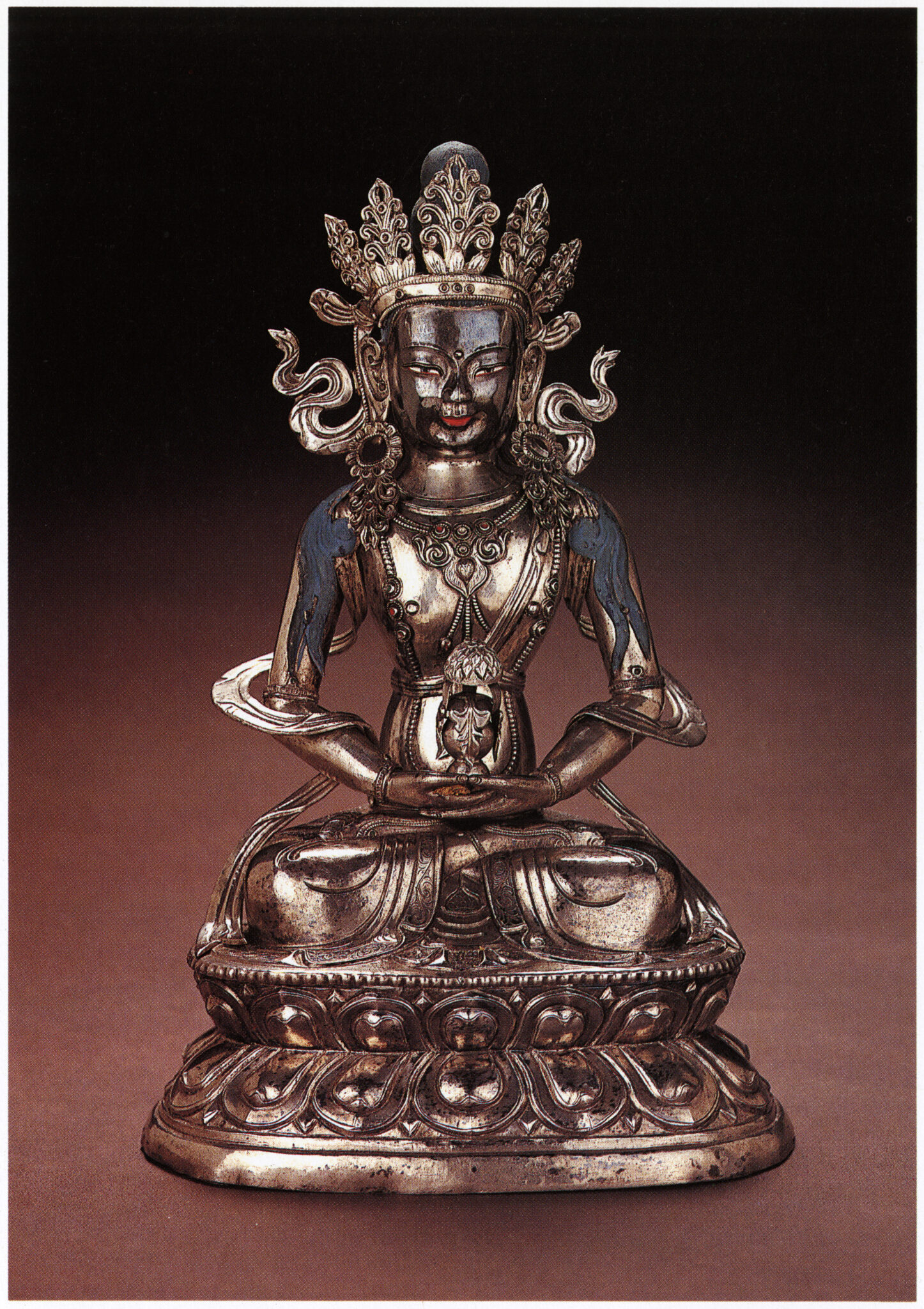 Silver statue depicting seated, crowned Buddha holding small vase in hands positioned in lap