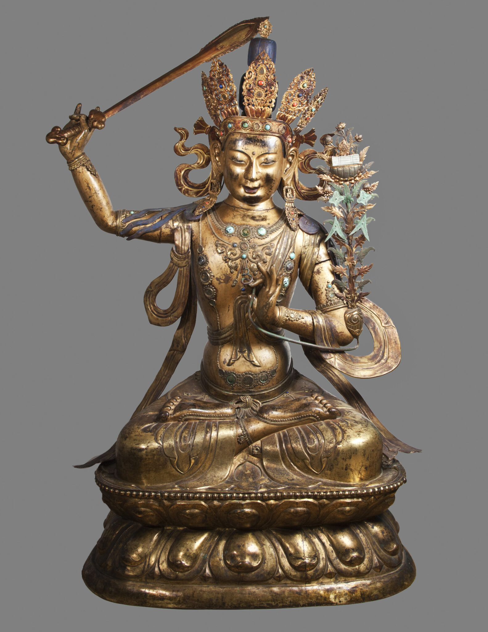Copper-colored statue depicting Bodhisattva raising sword with left arm, long-stemmed blossom at right shoulder