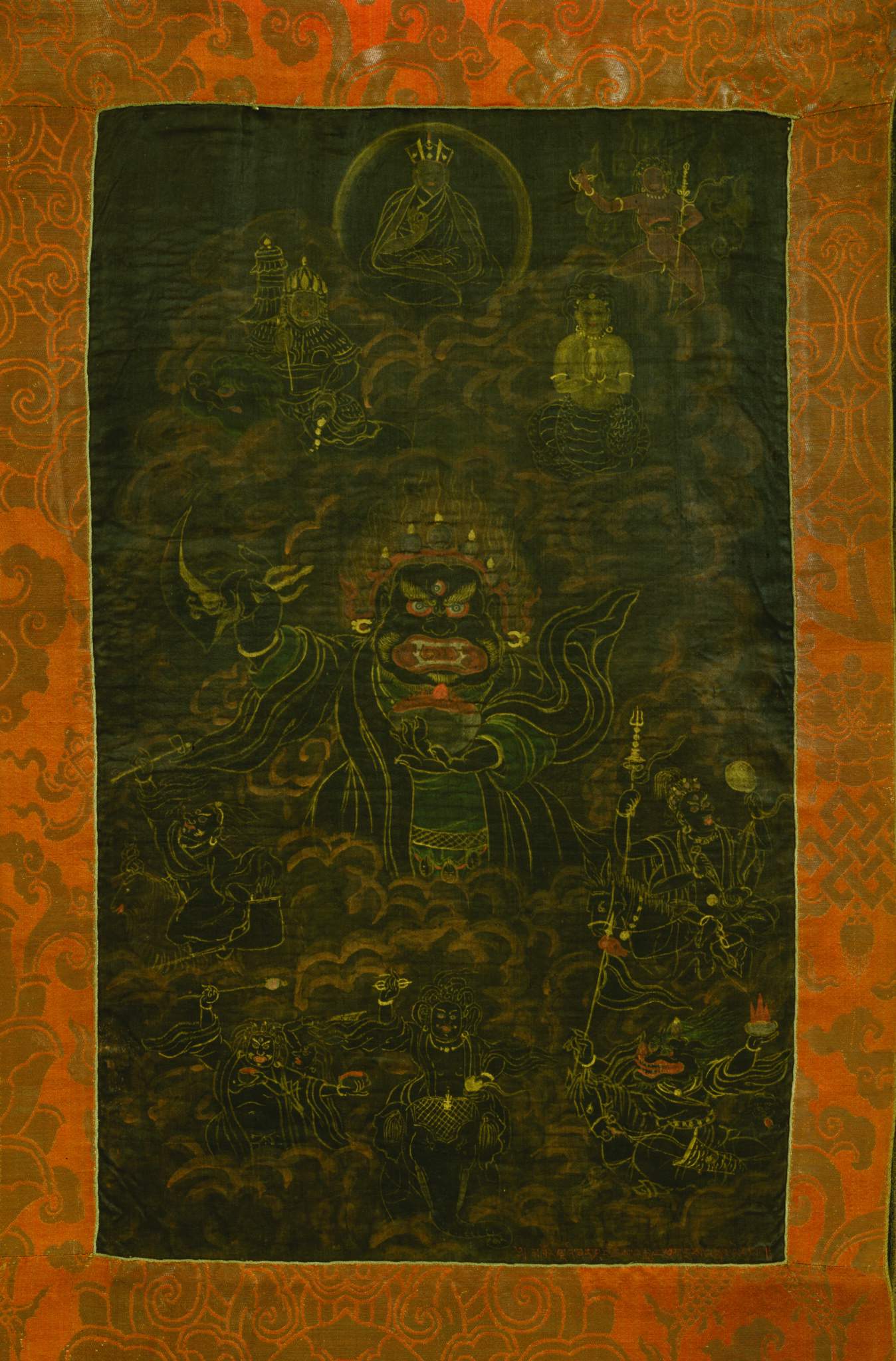Black and yellow painting mounted on golden brocade depicting fearsome deity dressed in swirling cloak
