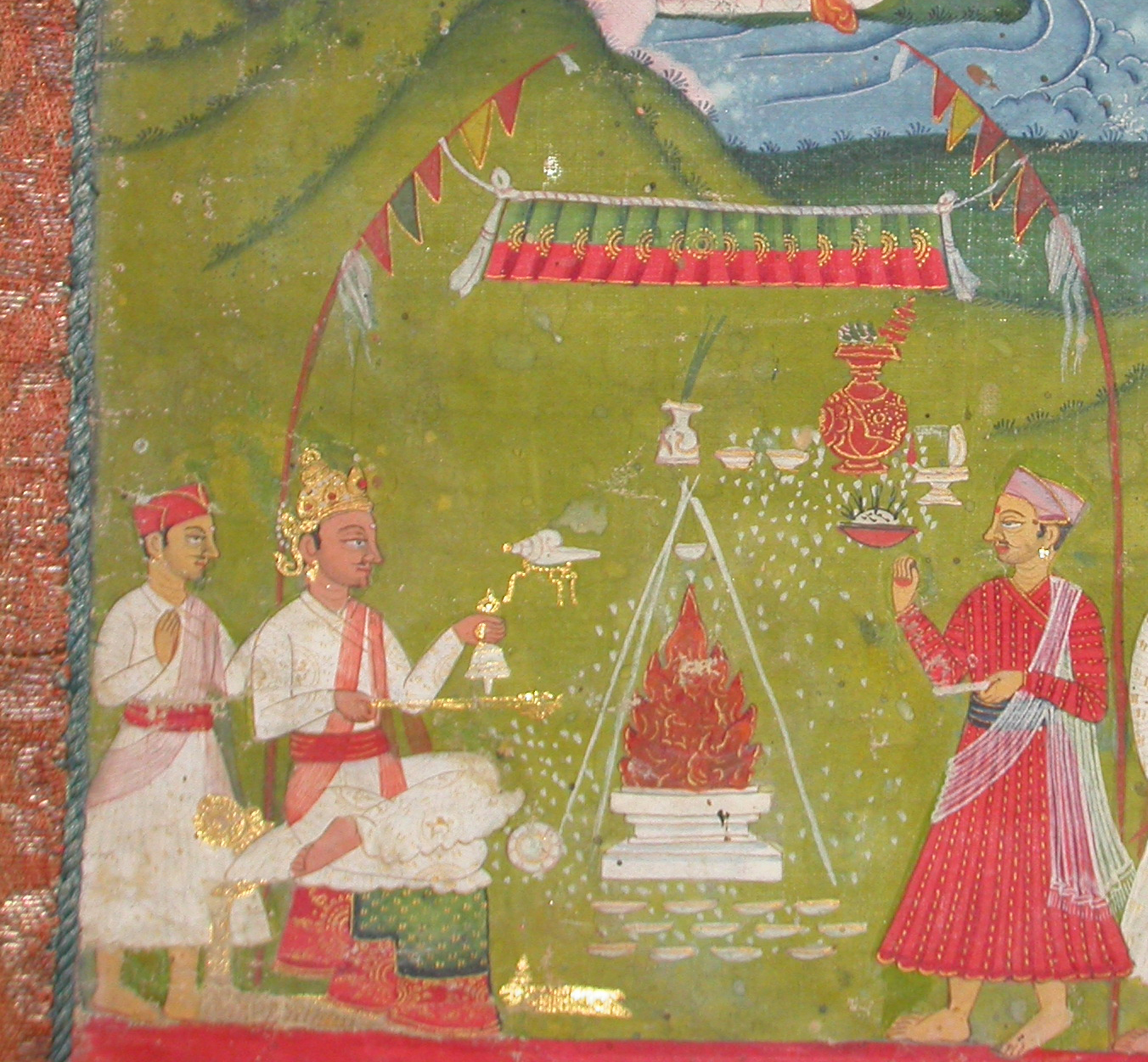 Priest in red garment at right casts white material into fire at center, with white-robed attendants at left