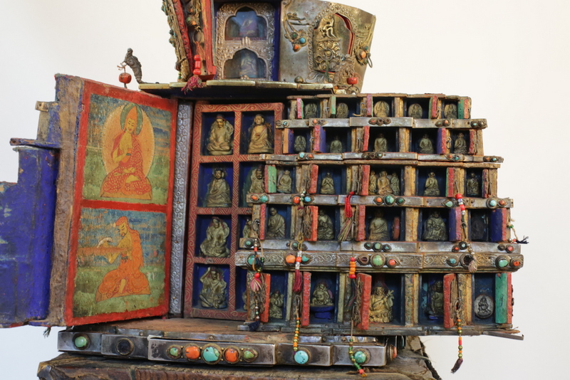Close view of religious implement with doors opened revealing dozens of portraits; decorated with pigments and stones