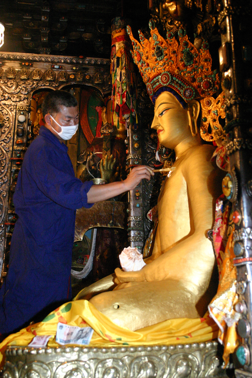 Man dressed in blue work clothes and face mask applies paint to golden statue of Buddha