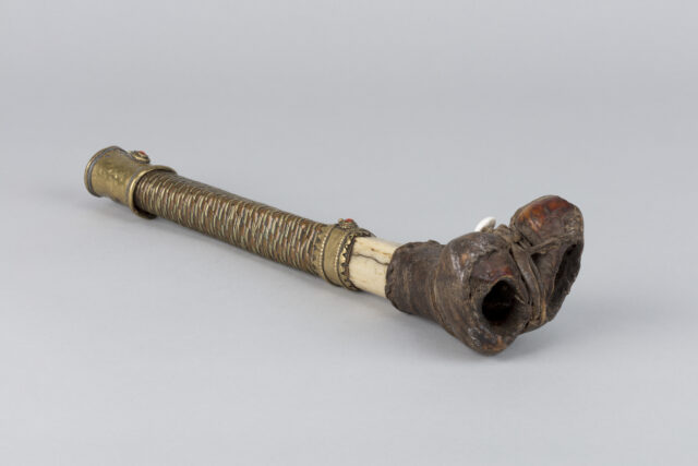 Wind instrument made from human leg bone; shaft covered in copper sheath, joint wrapped with natural material