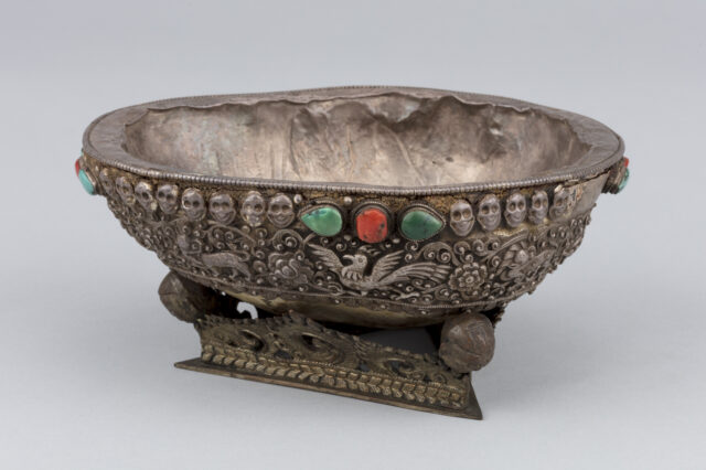 Side view of cup featuring bird with outstretched wings under blue-green and red stones