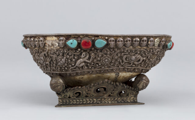 Side view of cup featuring band of silver decoration depicting animals amongst floral motifs and line of skulls