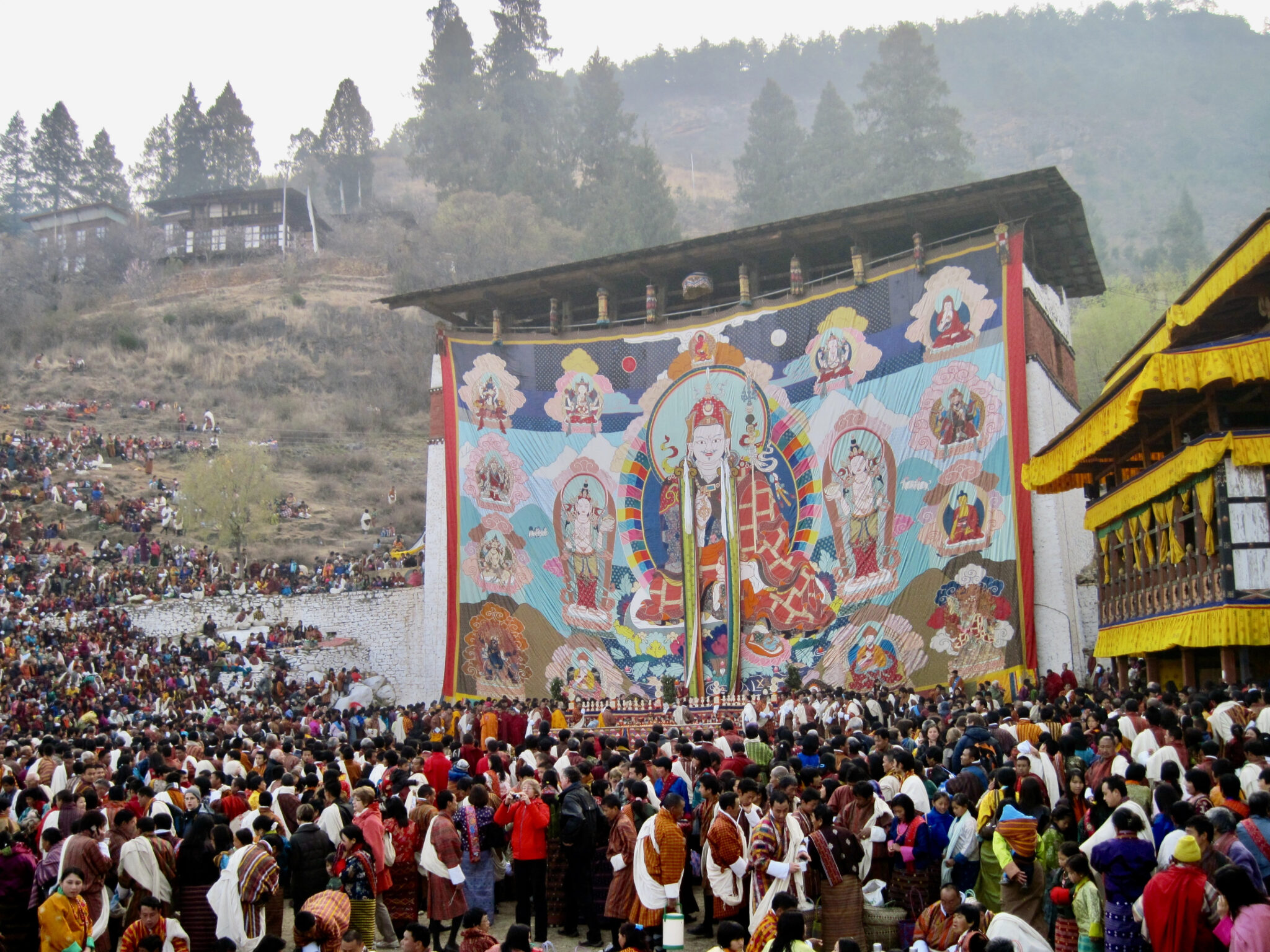 Monumental textile hung on the side of building before large crowd depicting Guru surrounded by portraits
