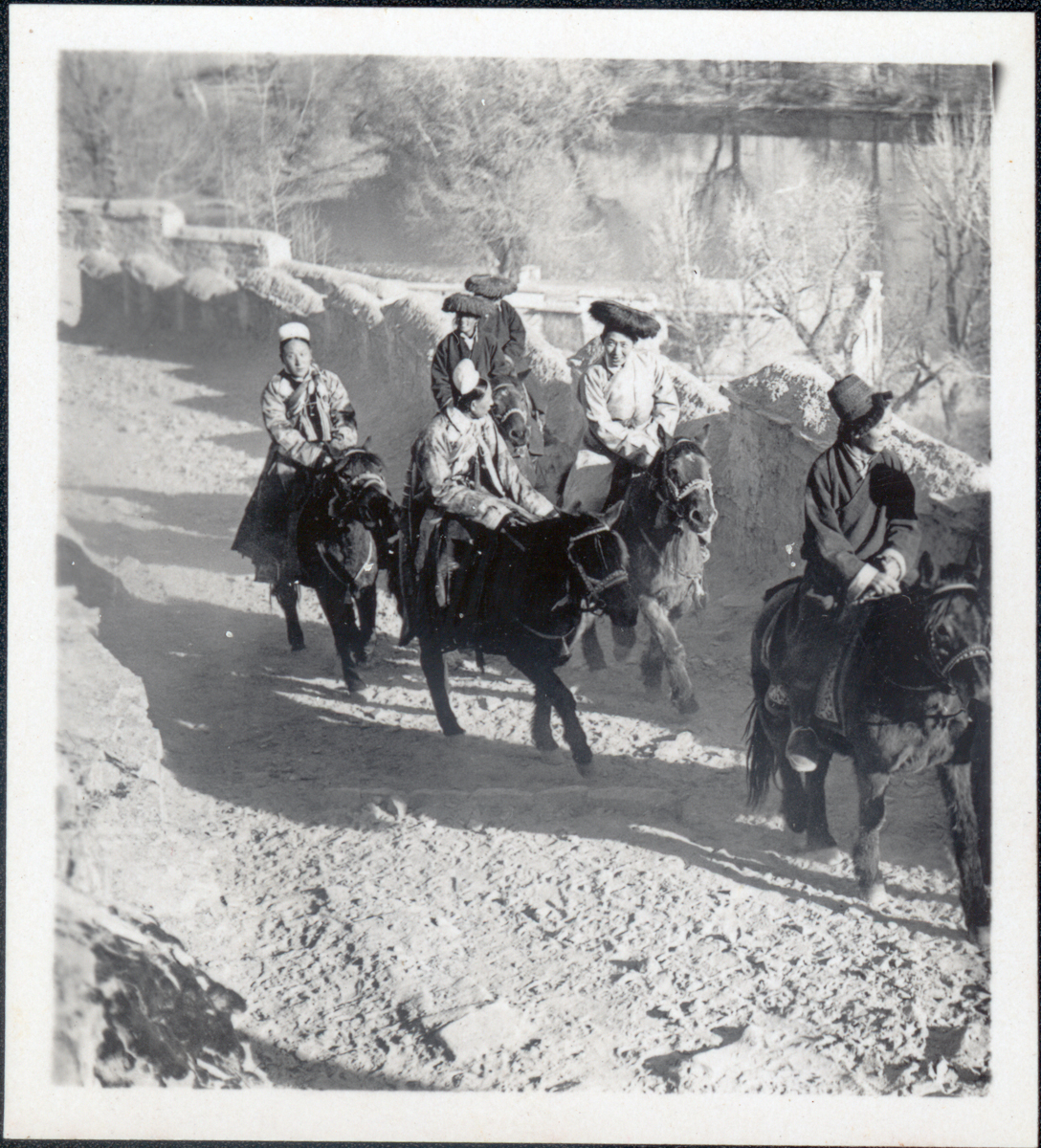 Black and white photograph of six officials riding on horseback up dusty hillside path