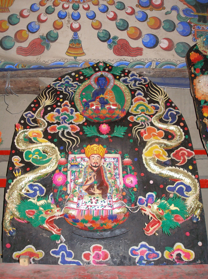 Colorful butter sculpture depicting Lama seated between two writhing dragons underneath Buddha with blue skin