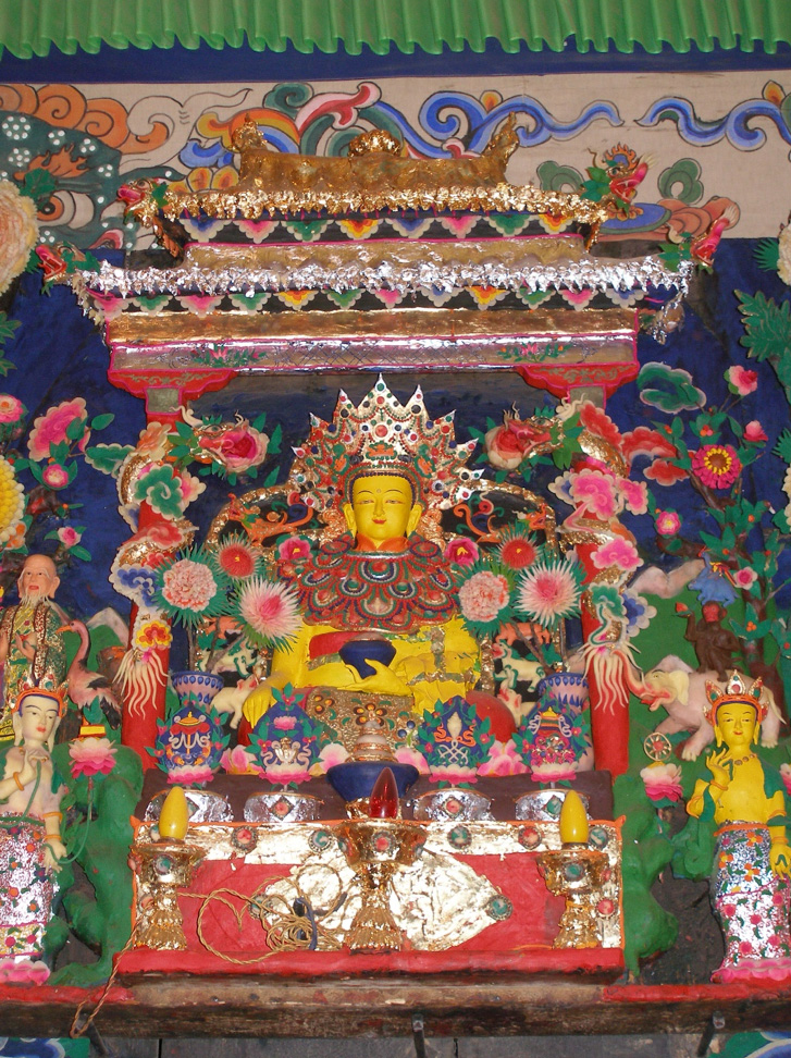 Colorful butter sculpture depicting Buddha seated underneath richly decorated canopy, flanked by attendants
