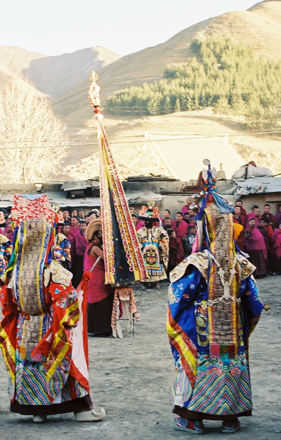 Lamas and performers in sumptuous costumes gather around tall triangular implement topped by stylized skull