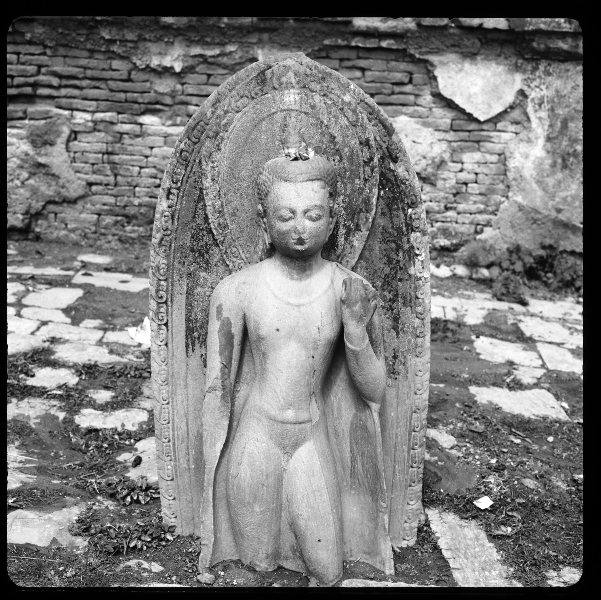 Black and white photograph of sculpture depicting Buddha standing in contrapposto; legs below knees are lost