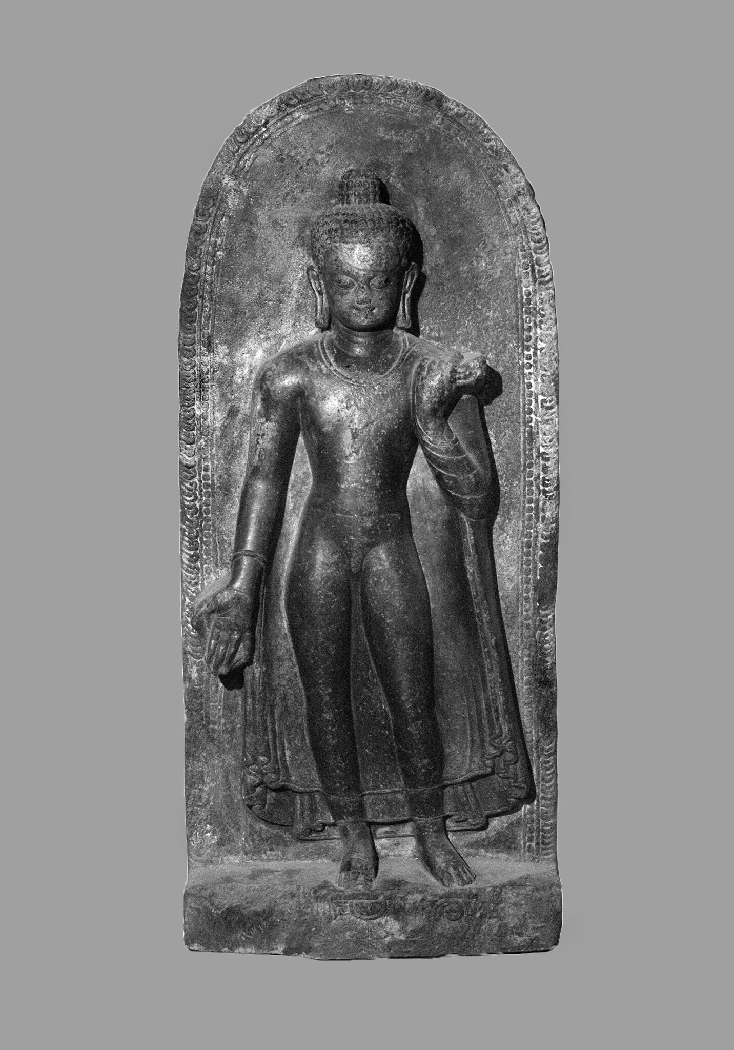 Black and white photograph of relief sculpture depicting Buddha wearing sheer tunic standing in contrapposto
