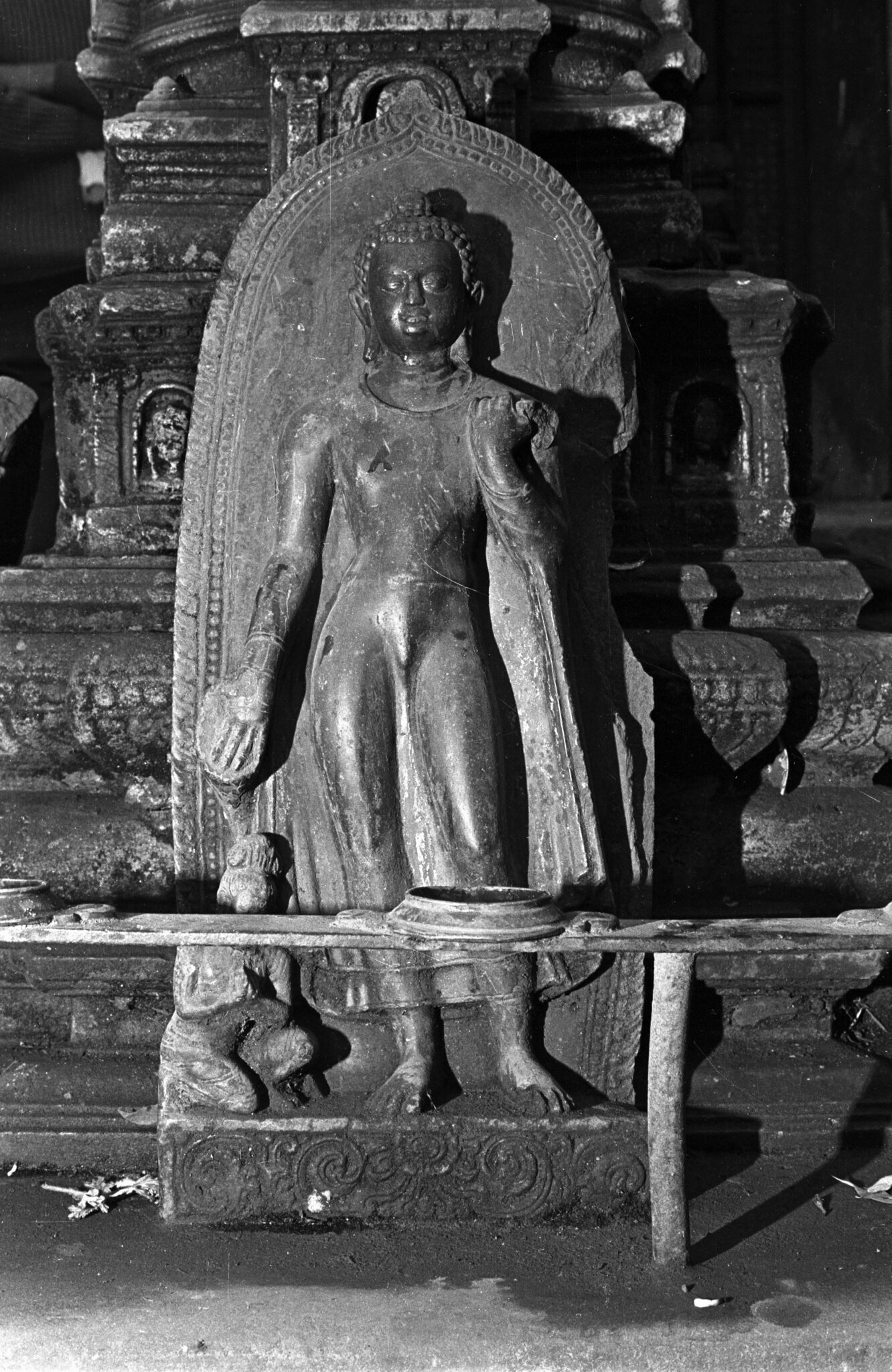 Black and white photograph of relief sculpture depicting Buddha and attendant situated before tiered architectonic sculpture