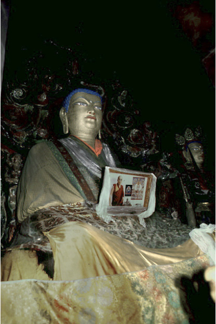 View from below of monumental Buddha seated in cross-legged position with photograph in lap