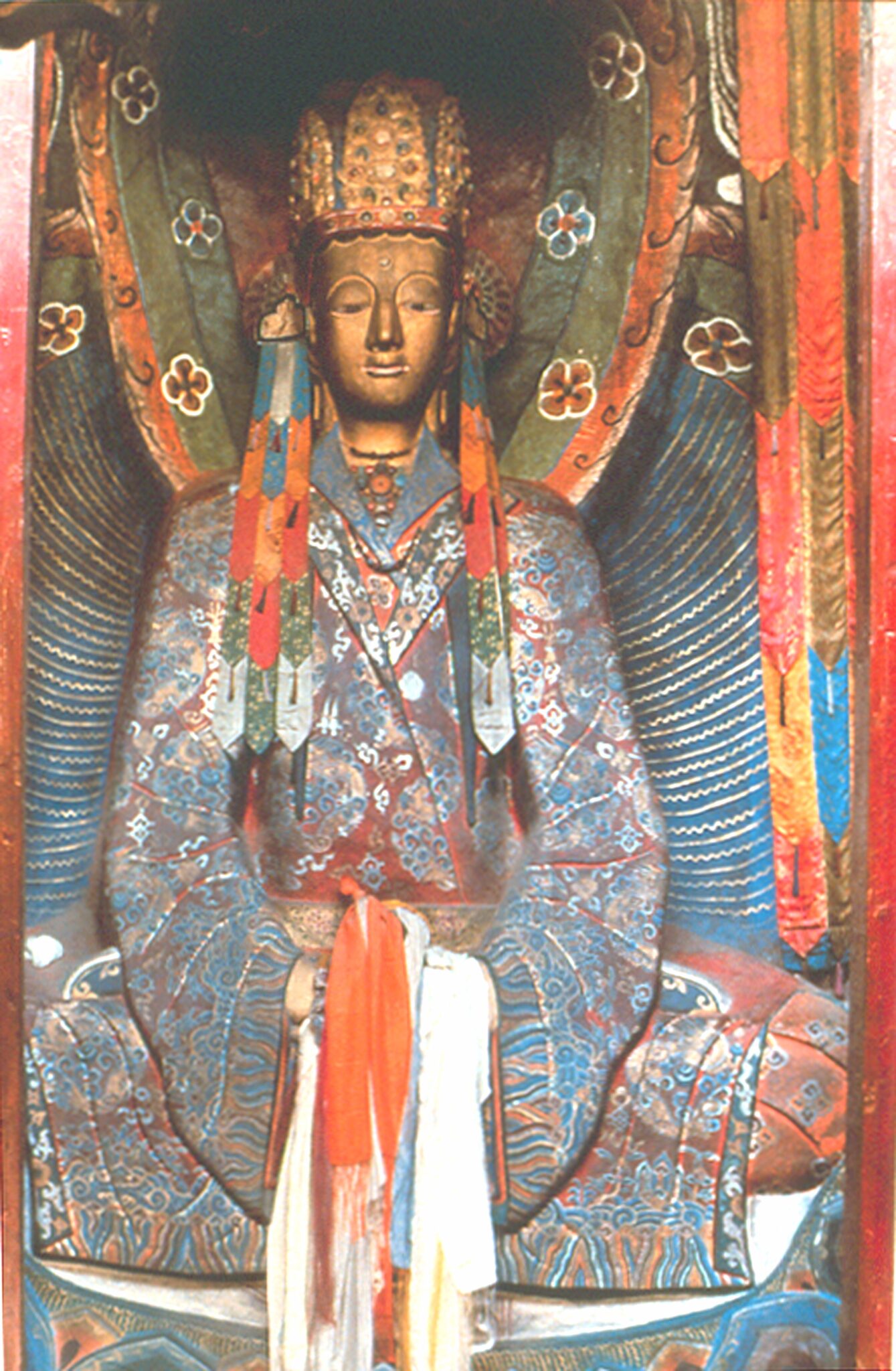 Seated Buddha wearing patterned robe in stone relief decorated with paint and textiles
