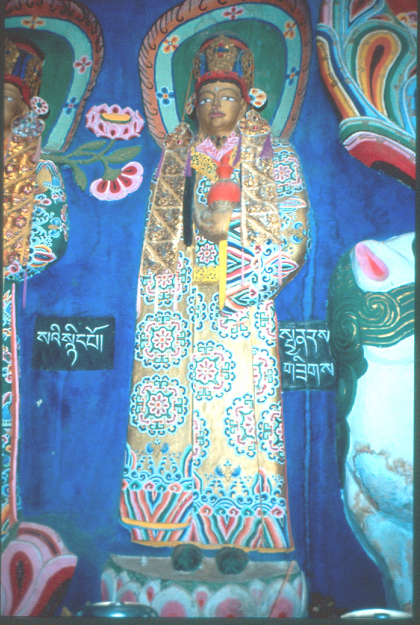 Statue of Bodhisattva wearing gold robe with rosette pattern standing against deep-blue wall