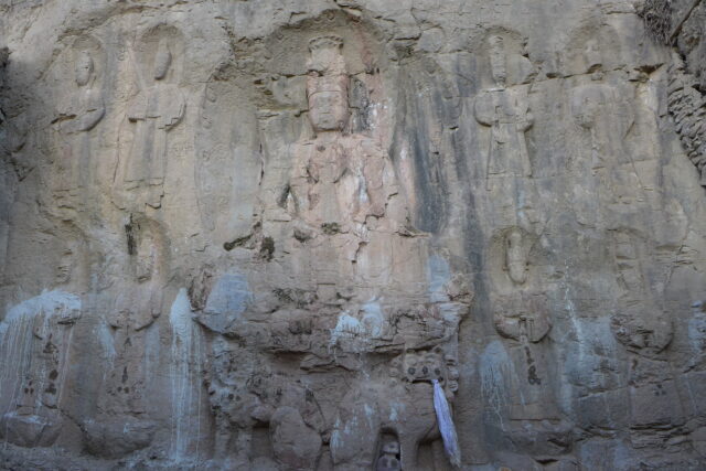 Weathered brown stone relief of Buddha seated on throne and flanked by eight standing Bodhisattvas