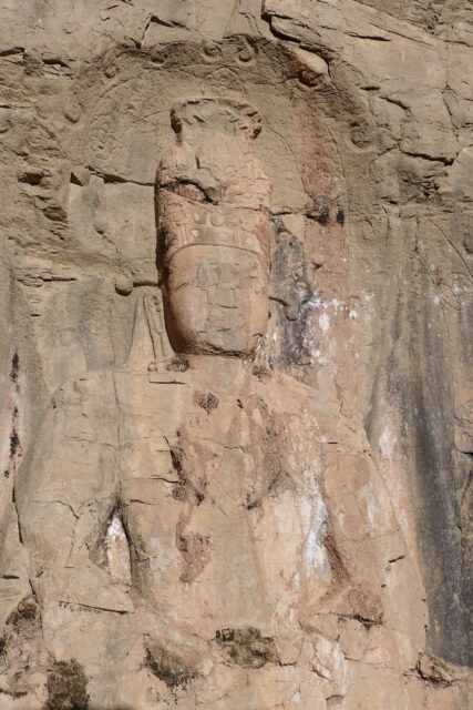 Medium view of upper body of Buddha in weathered orange-brown stone relief