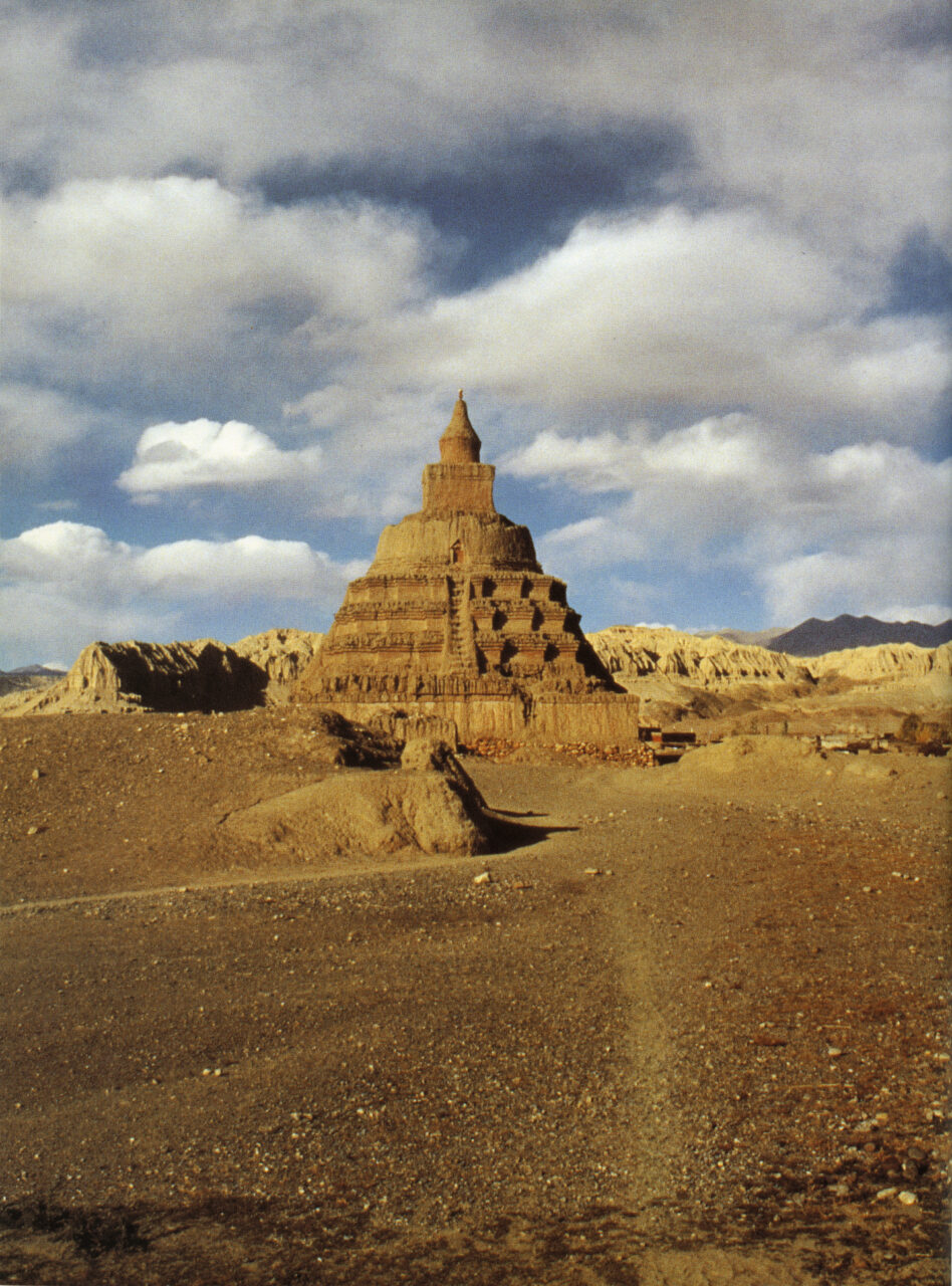 Conical, tiered structure rises into ruddy sky and matches dusky orange-red color of surrounding landscape