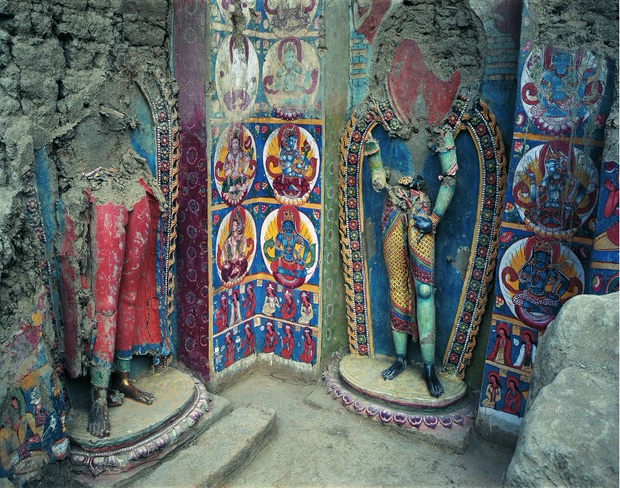 Two statues of deities missing their torsos and heads stand amid brightly painted murals depicting deities