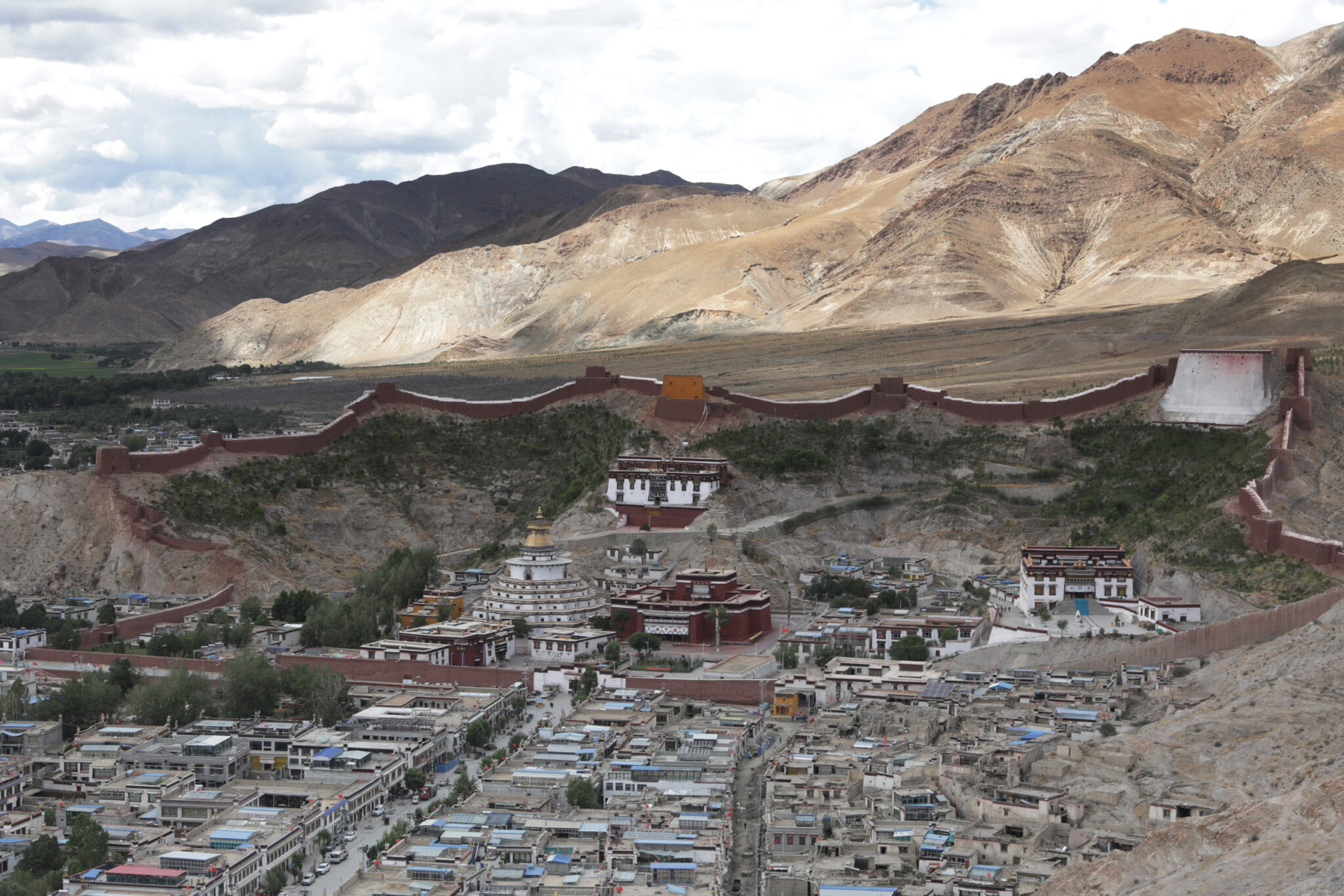 Aerial view of village dominated by religious complex surrounded by red wall situated in mountain valley