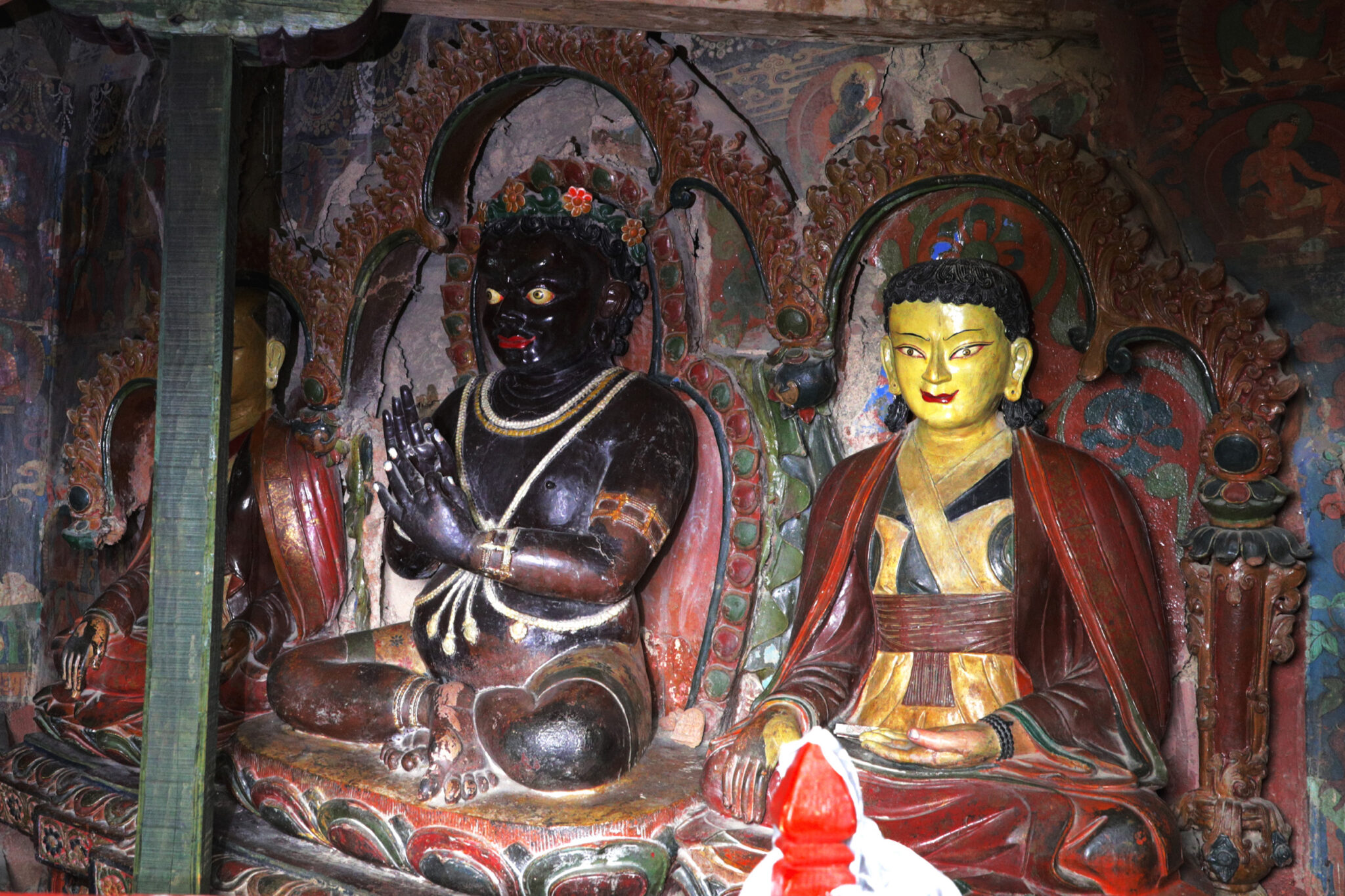 Two polychrome statues depicting seated figures: at left, Yogi with hands in mudras; at right, red-robed spiritual leader
