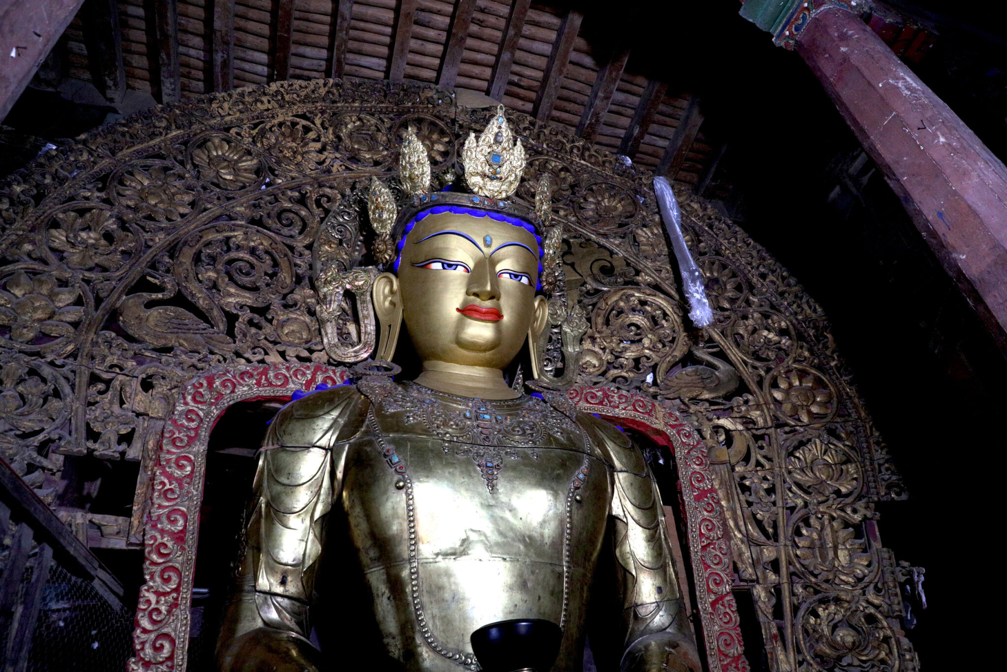 View from below of upper body of monumental golden Buddha before densely wrought open nimbus