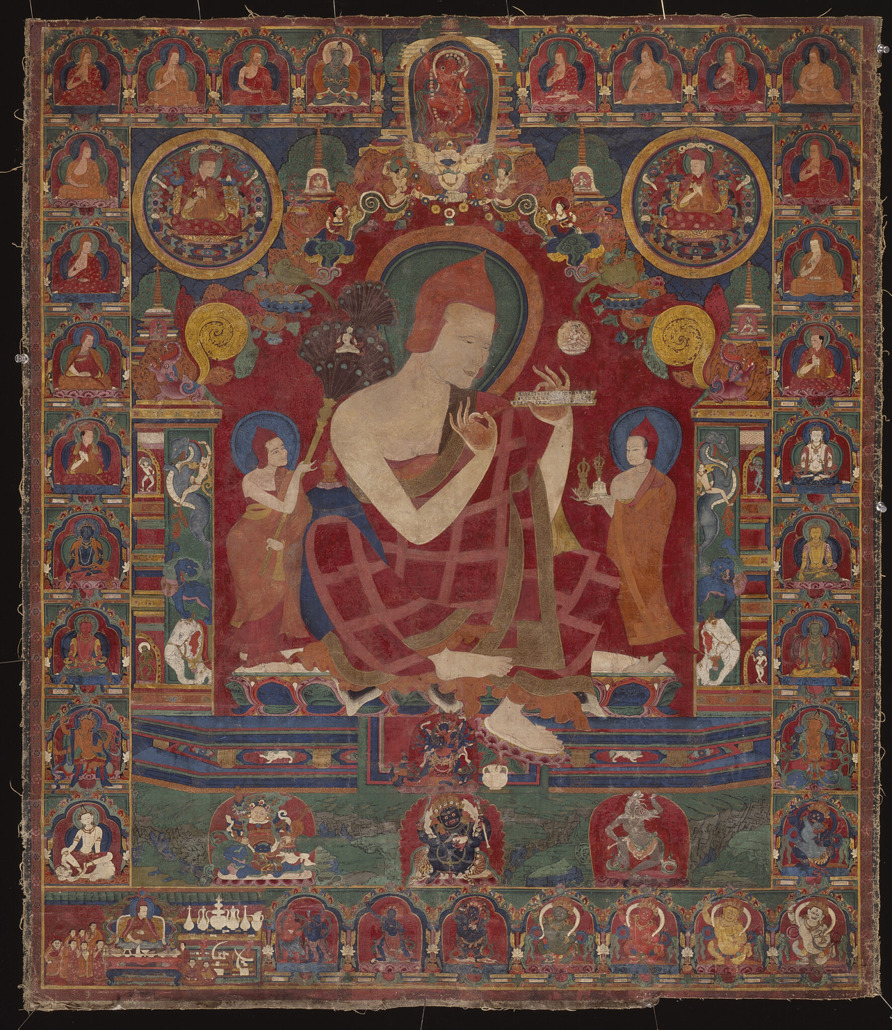 Enlightened teacher holds implement in hands at chest; flanked by attendants and surrounded by portrait border