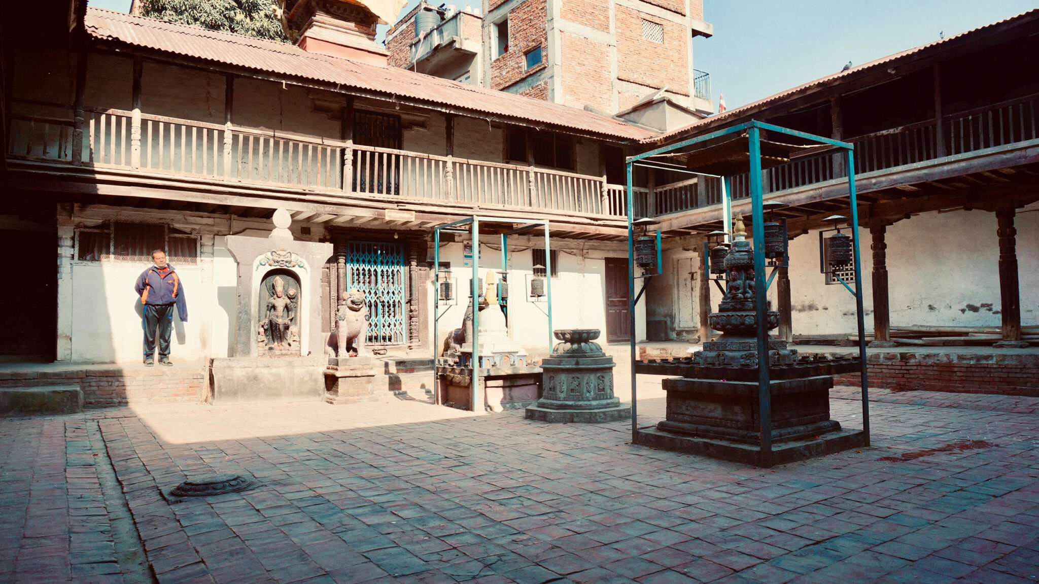 Courtyard featuring second-story loggia under sloping roofline; religious sculptures and implements at center of courtyard