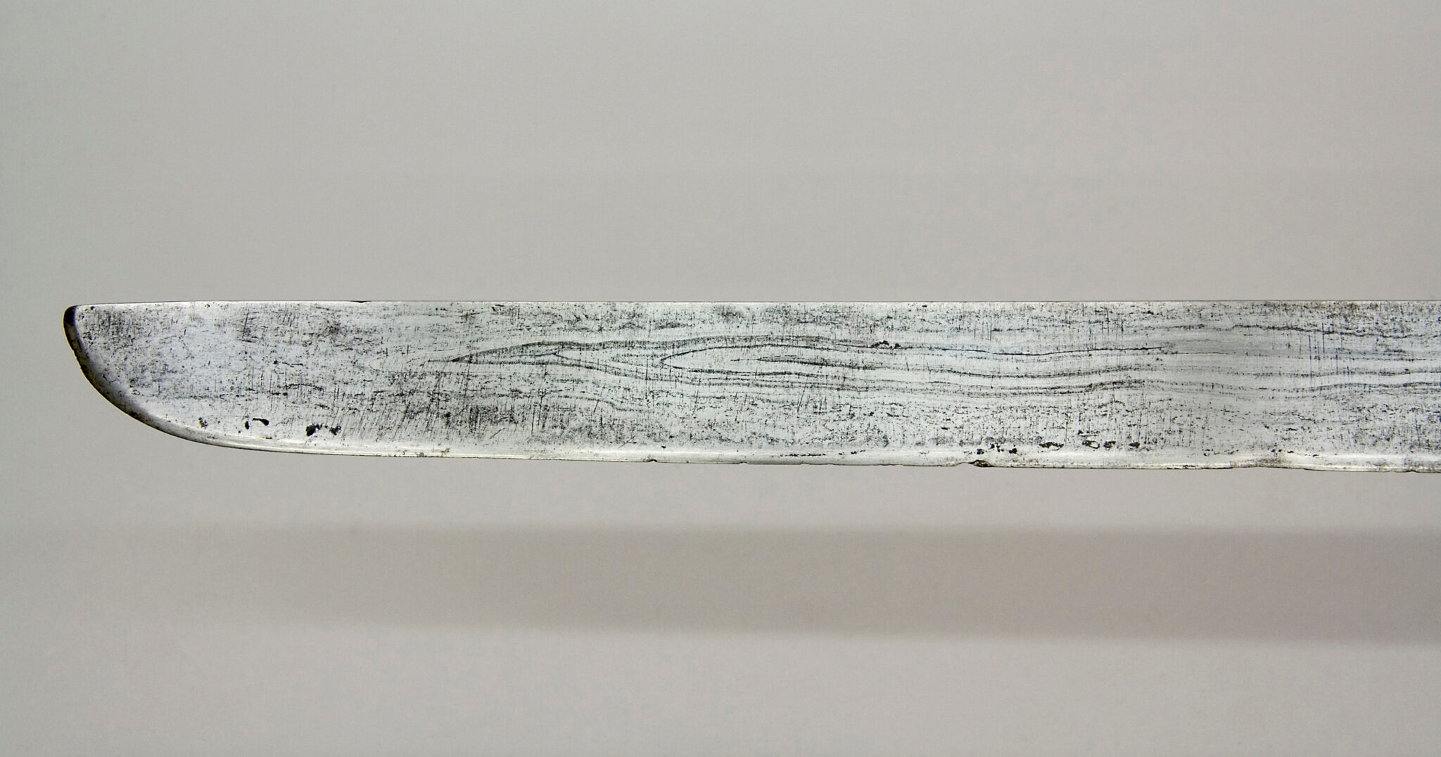 Close view of tip of thin silver-colored blade; forging pattern resembles wood grain