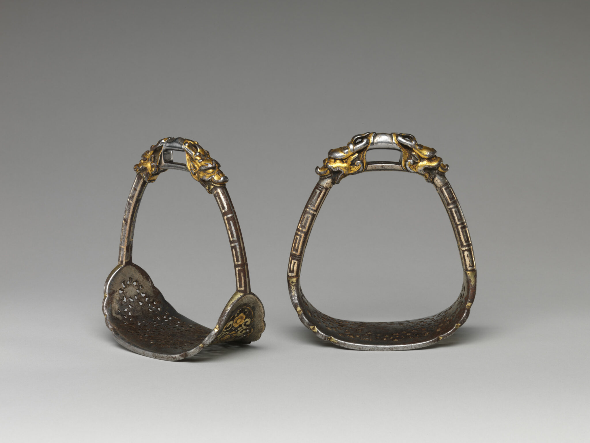 Two oblong silver stirrups featuring details and decoration in gold; footbeds pierced with small holes