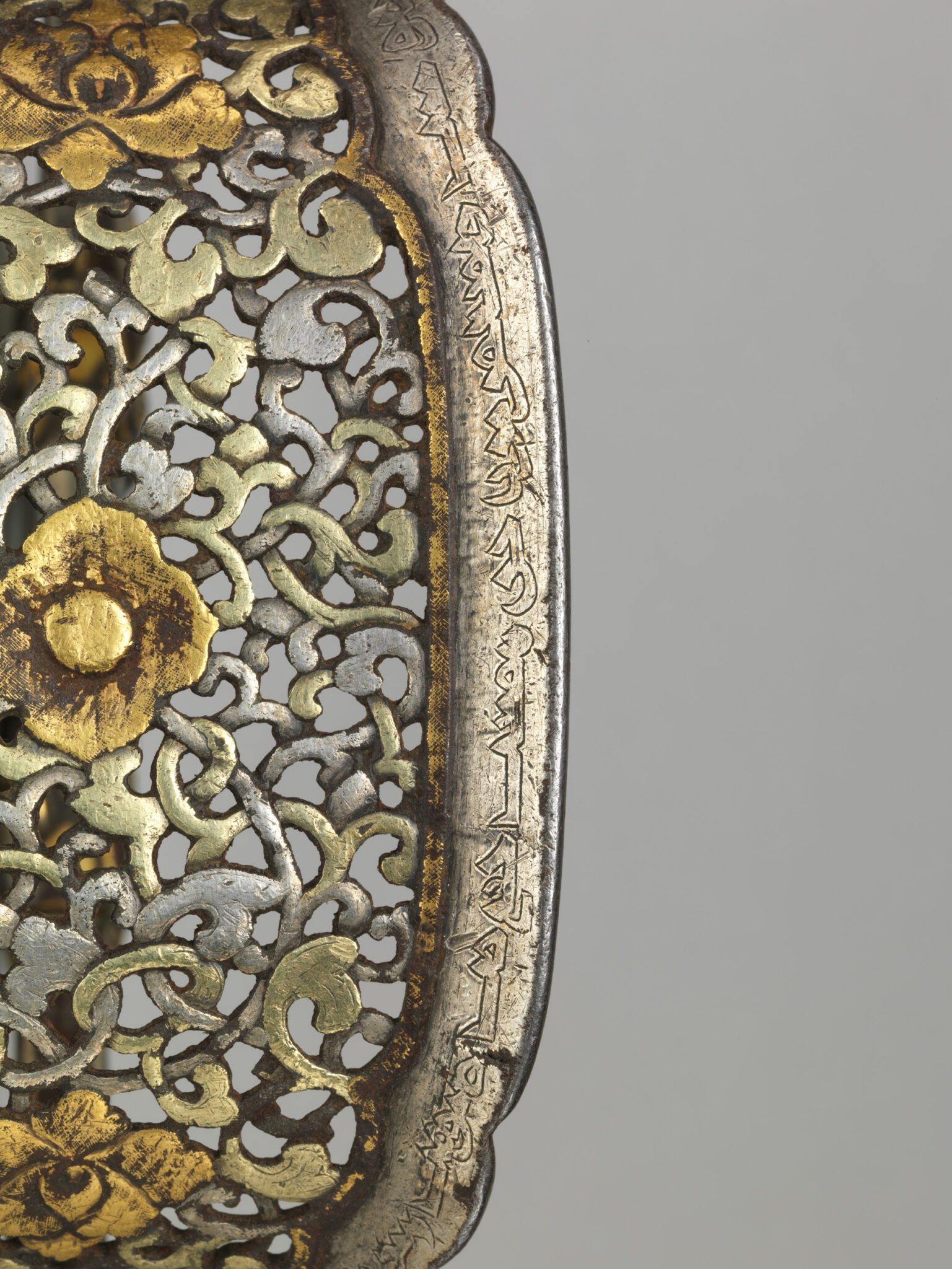 Close view of silver and gold stirrup: field of open-work floral motif bordered on right by Mongolian inscription