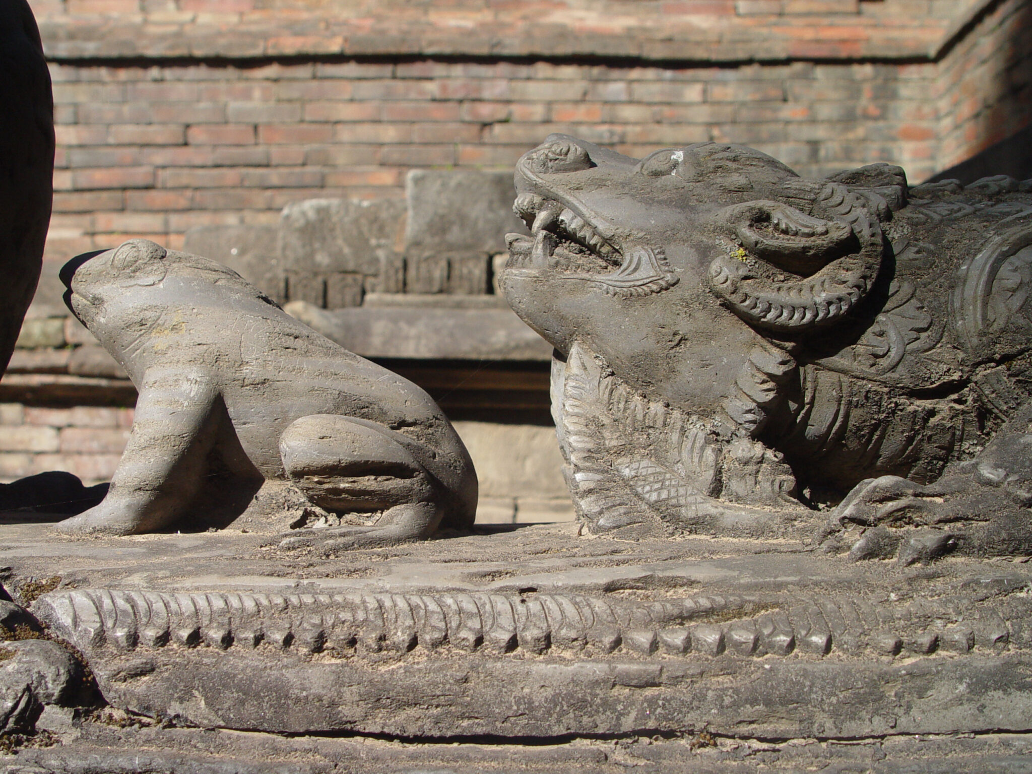 Two stone sculptures depicting animals: frog at left; horned, grinning beast at right
