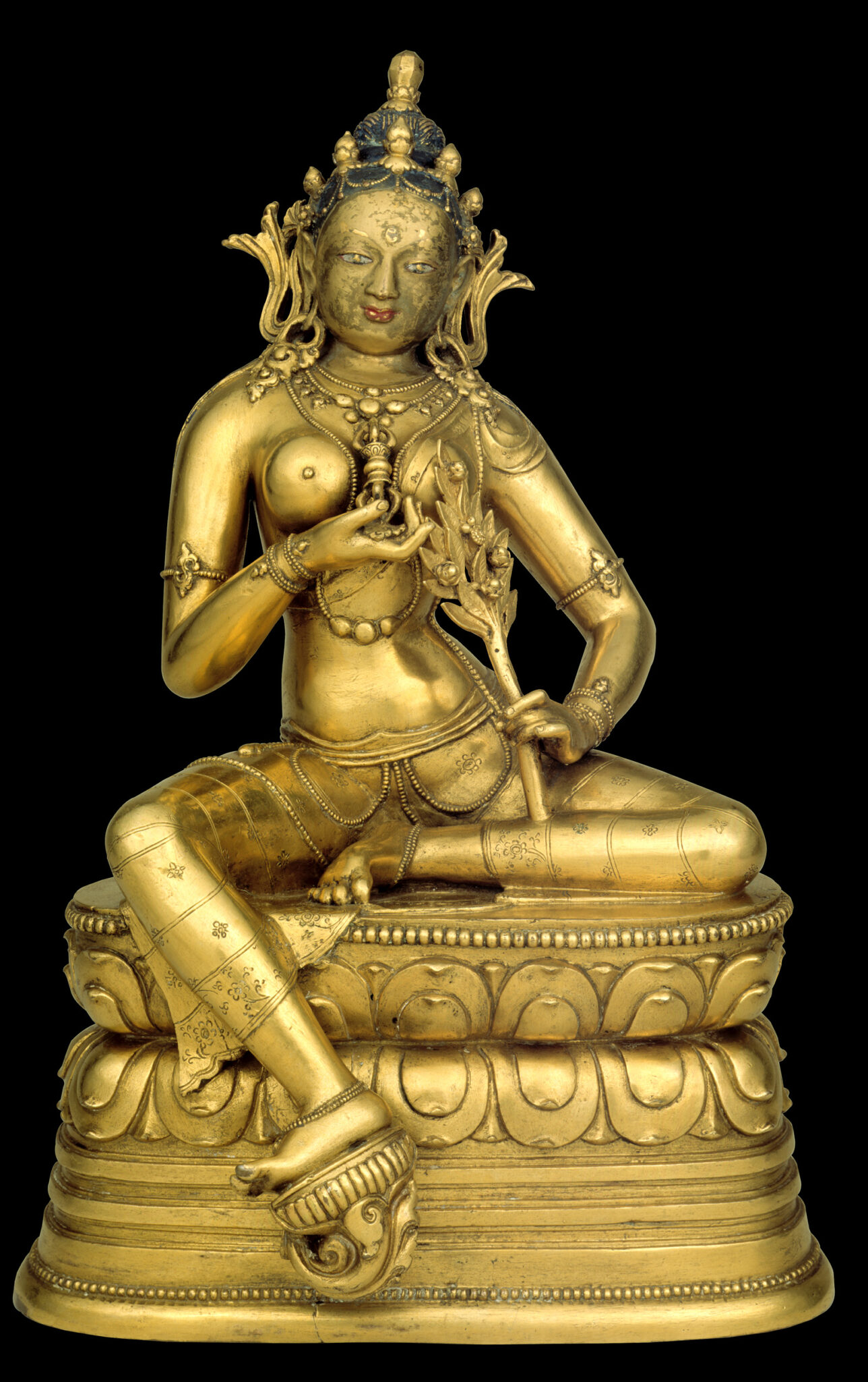 Golden statue depicting goddess seated on lotus pedestal holding vajra in left hand at chest
