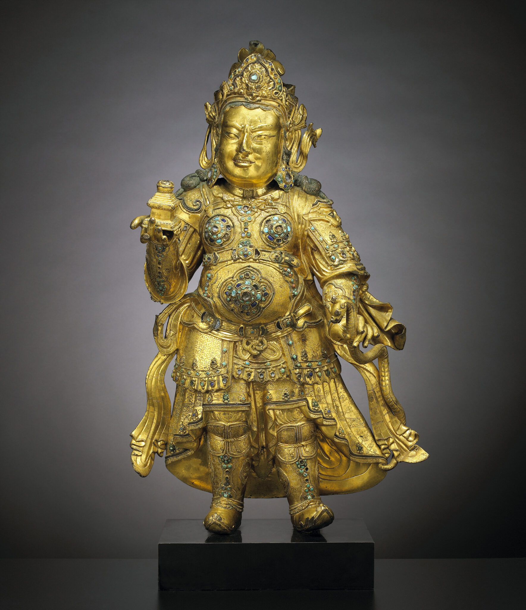 Golden deity statue wearing flowing robe inlaid with blue stones holding votive object in left hand