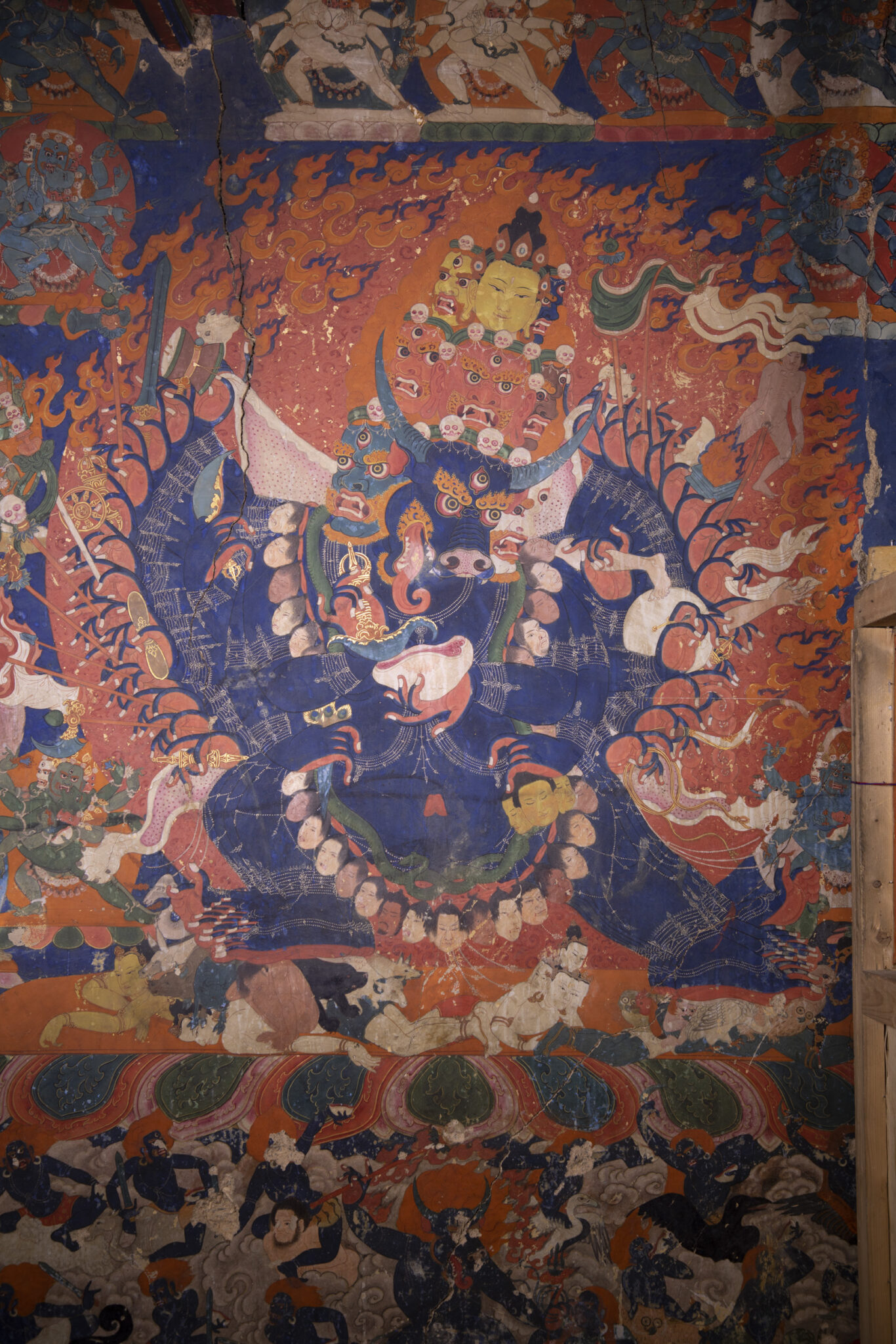 Blue-skinned, many-armed, cow- and human-headed deity in dynamic pose before fiery nimbus