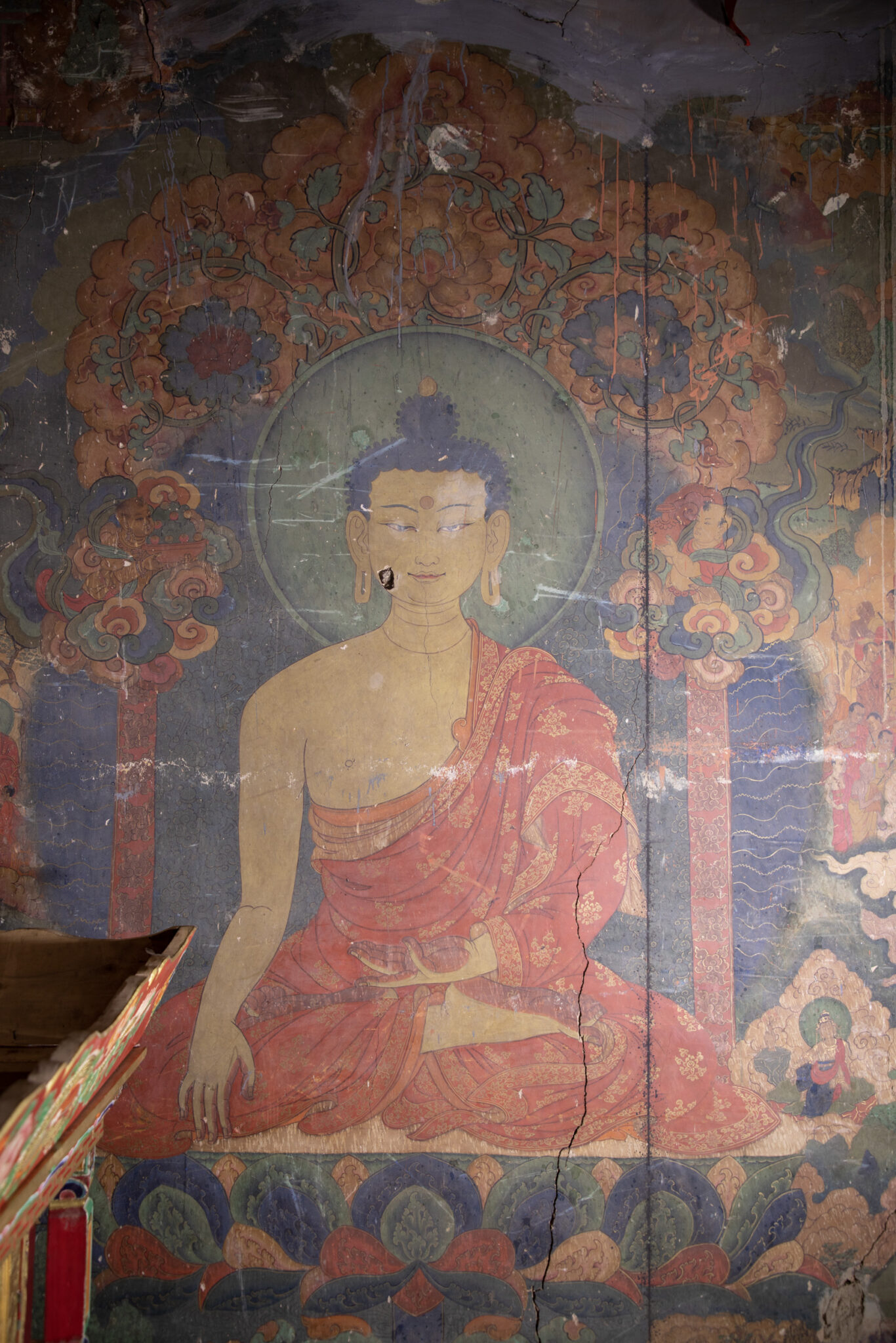 Mural depicting Buddha in sumptuous orange-red robe seated on throne featuring scrollwork backrest