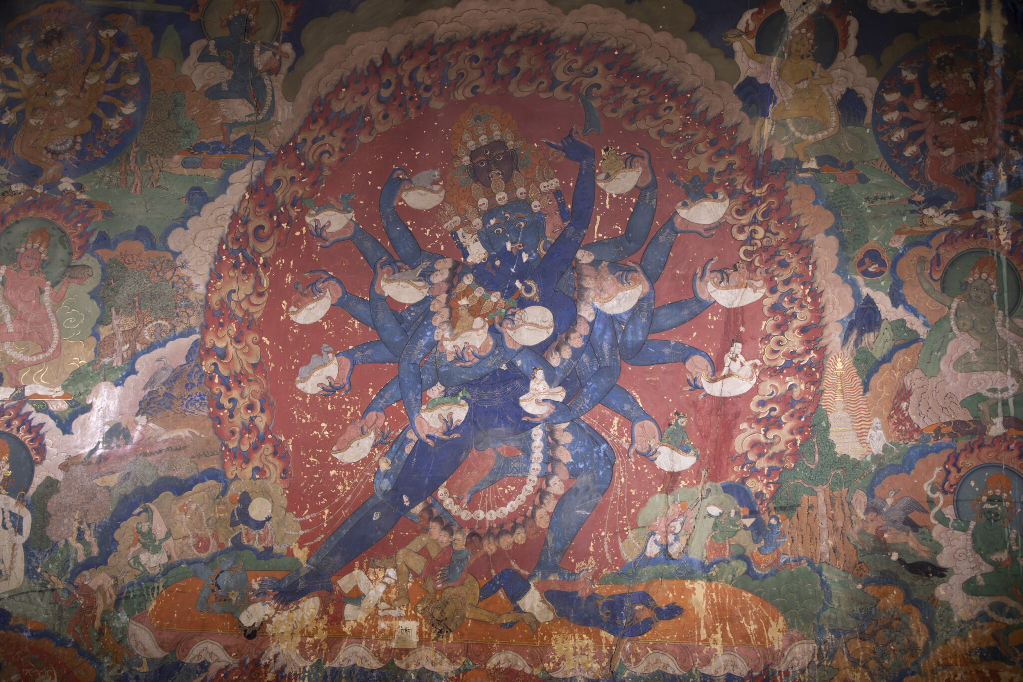Two blue-skinned, many-armed deities holding implements, locked in embrace before fiery nimbus