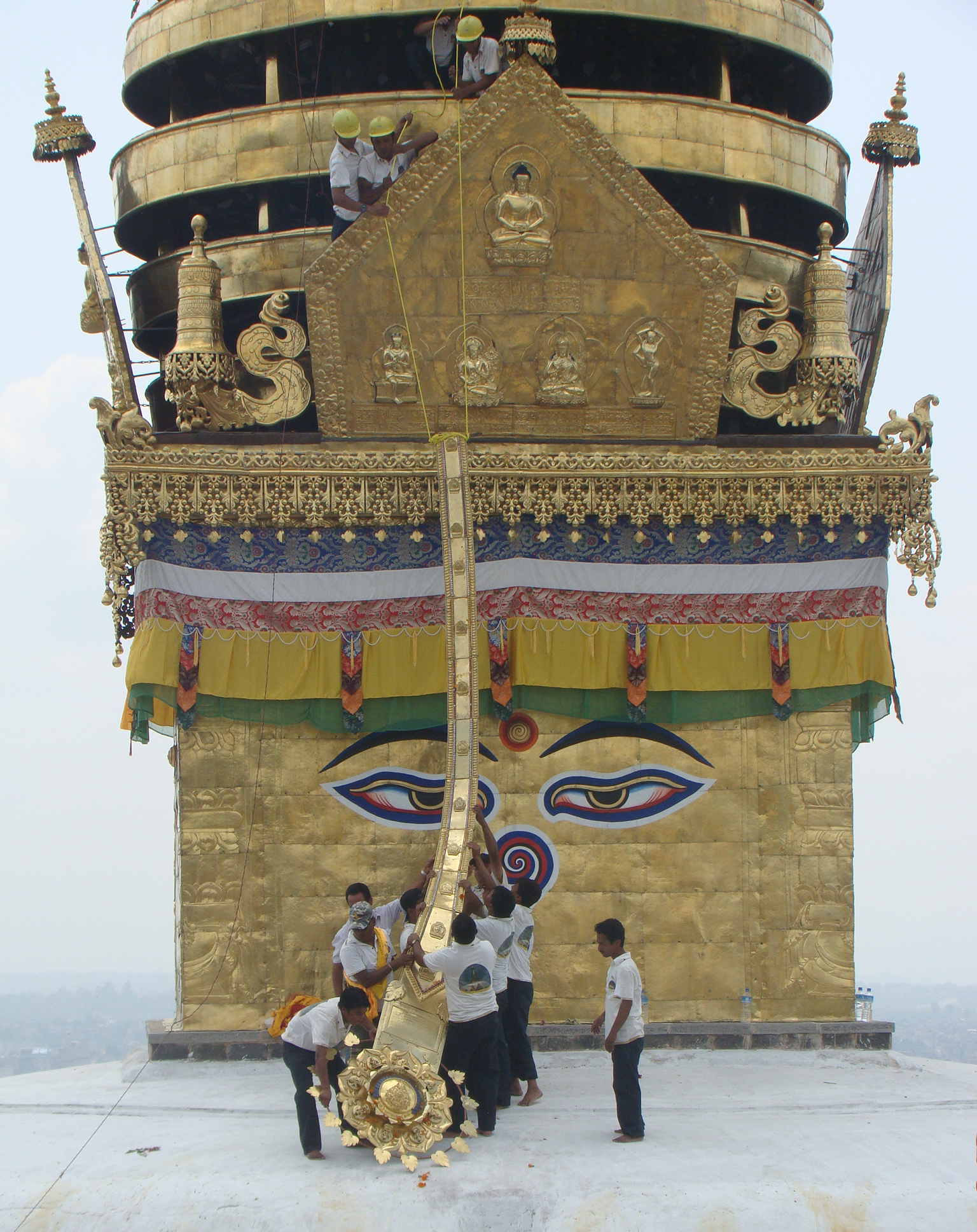 Golden stupa tower decorated with banners, filigree, and painted set of eyes with group of people at its base