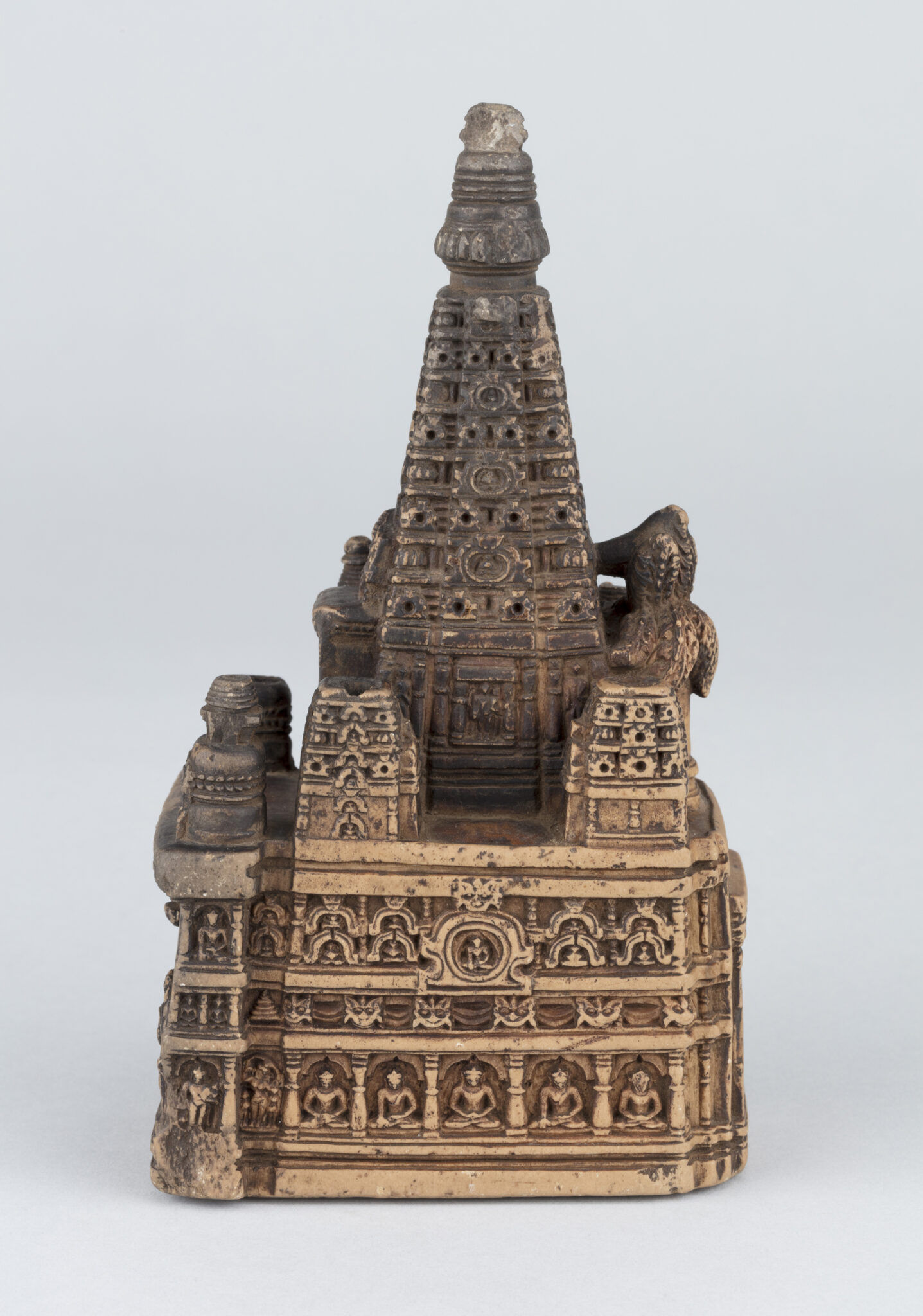 Side view of miniature architectural model with register of seated Buddhas at base and slender tapered roof