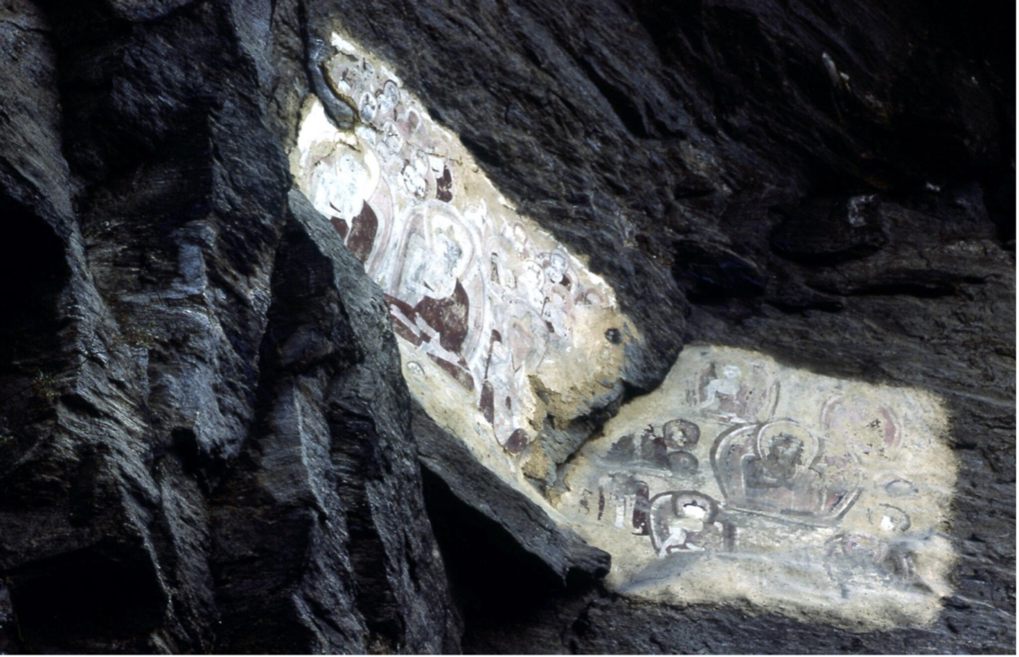 Photograph of faded image depicting deities painted on white material applied to face of craggy rock