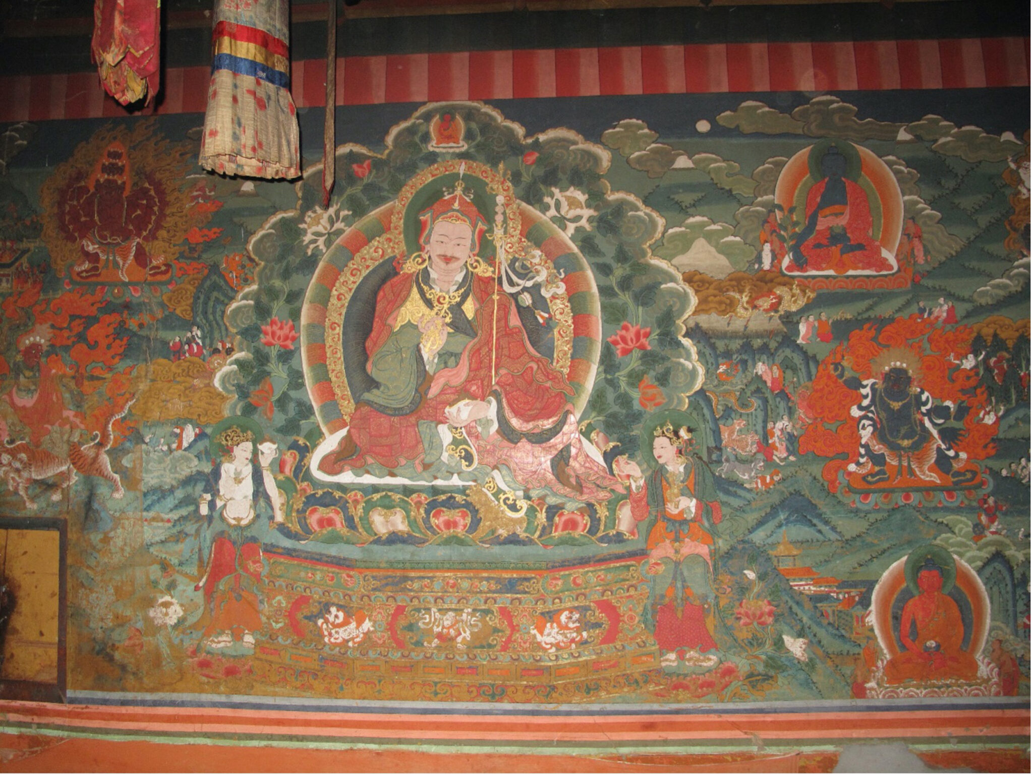 Mural depicting Guru holding staff, seated before flowery nimbus, flanked by attendants and deity portraits