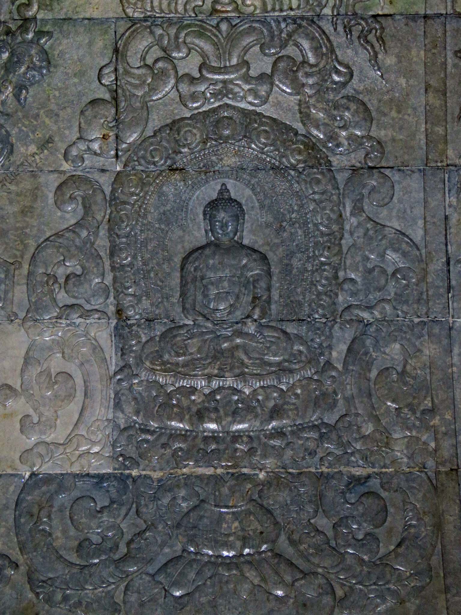 Relief carving depicting Buddha seated on lotus pedestal supported and enclosed by scrollwork motif