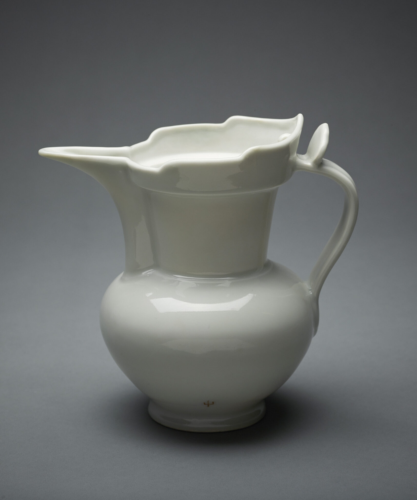 Glazed, milky-white porcelain pitcher with crown-shaped rim; handle features ovoid thumb rest